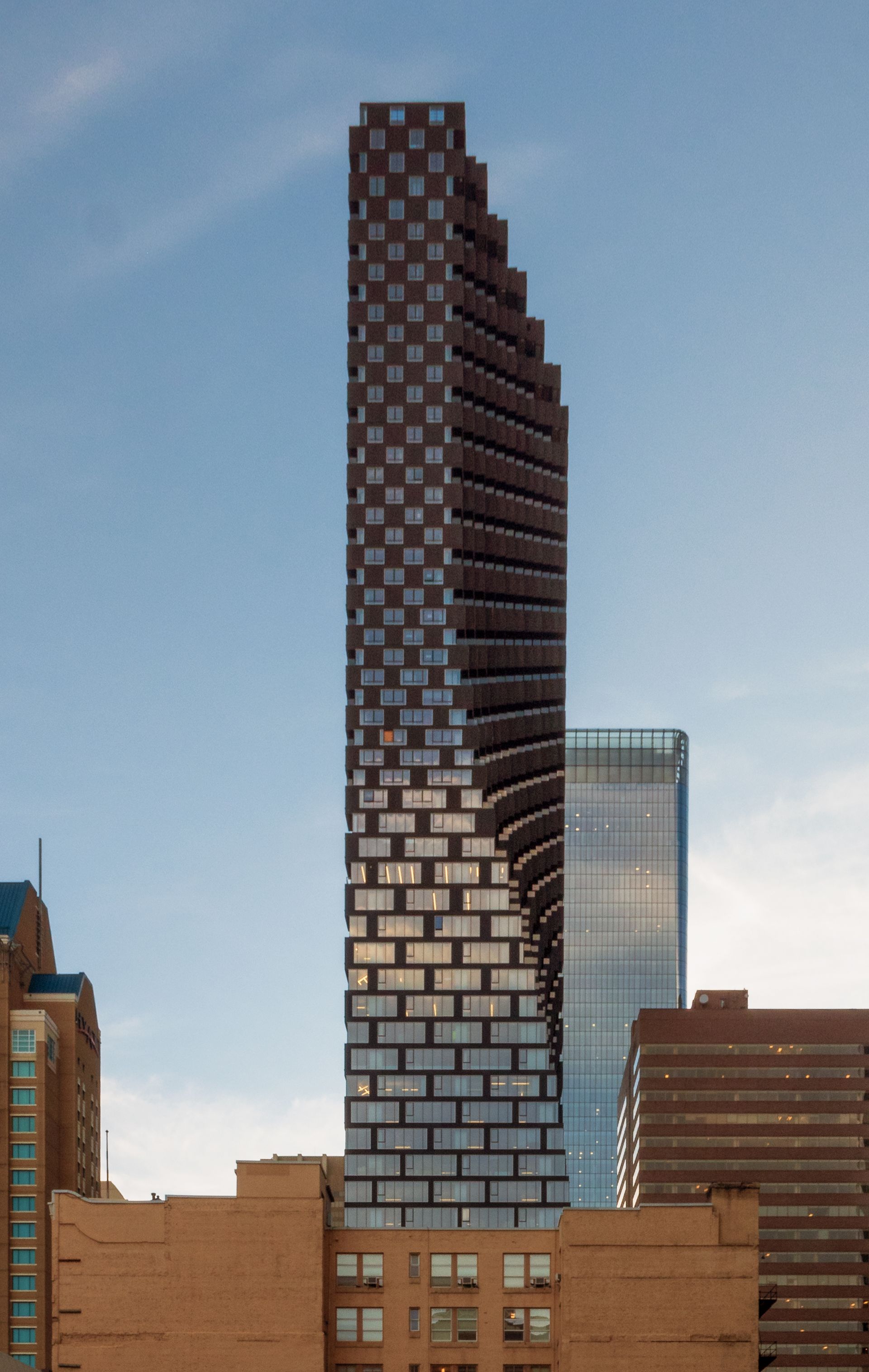 Tall checkered skyscraper against a blue sky, flanked by other buildings in a city.