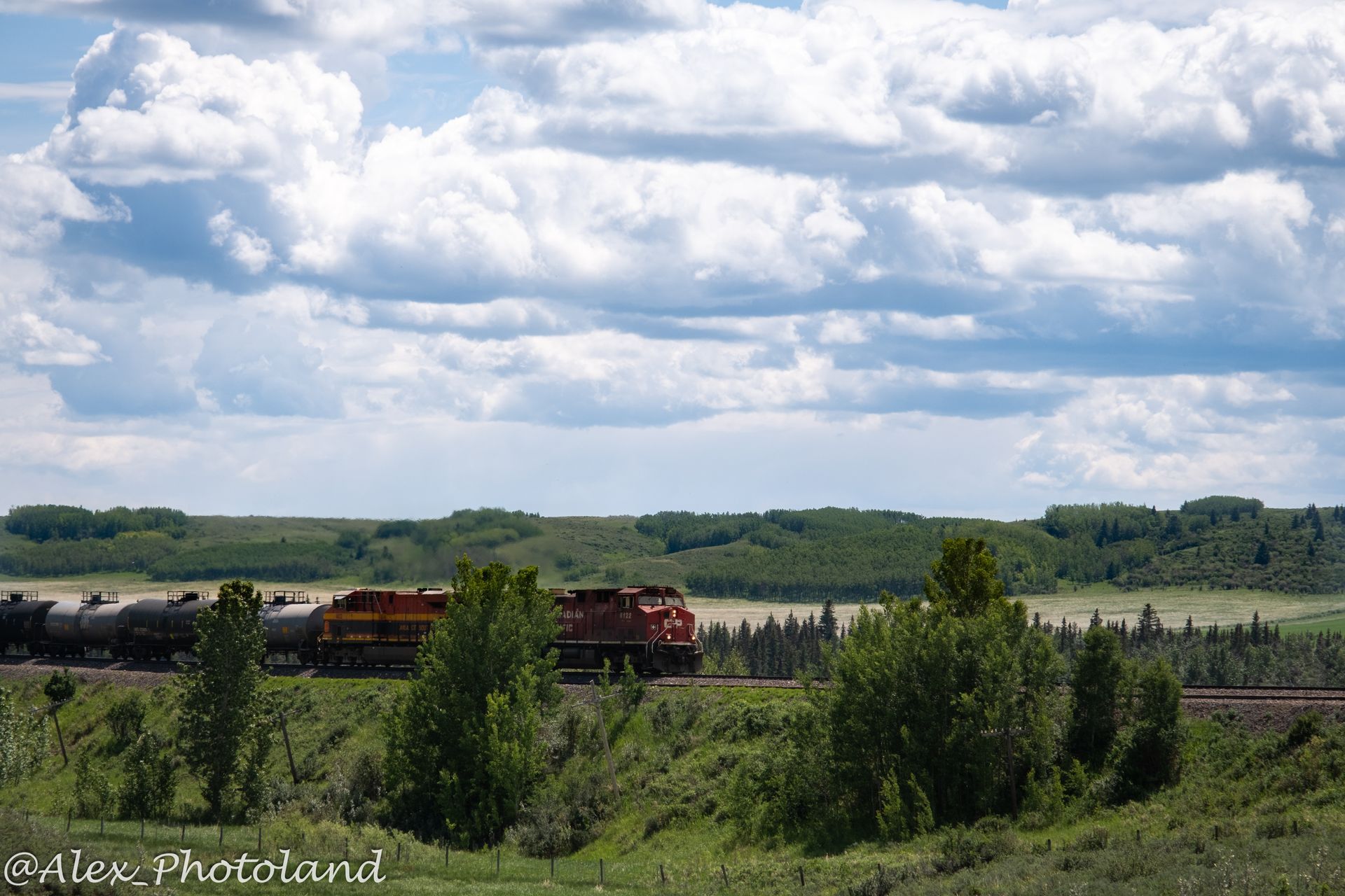Train traveling through a green landscape under a cloudy blue sky.