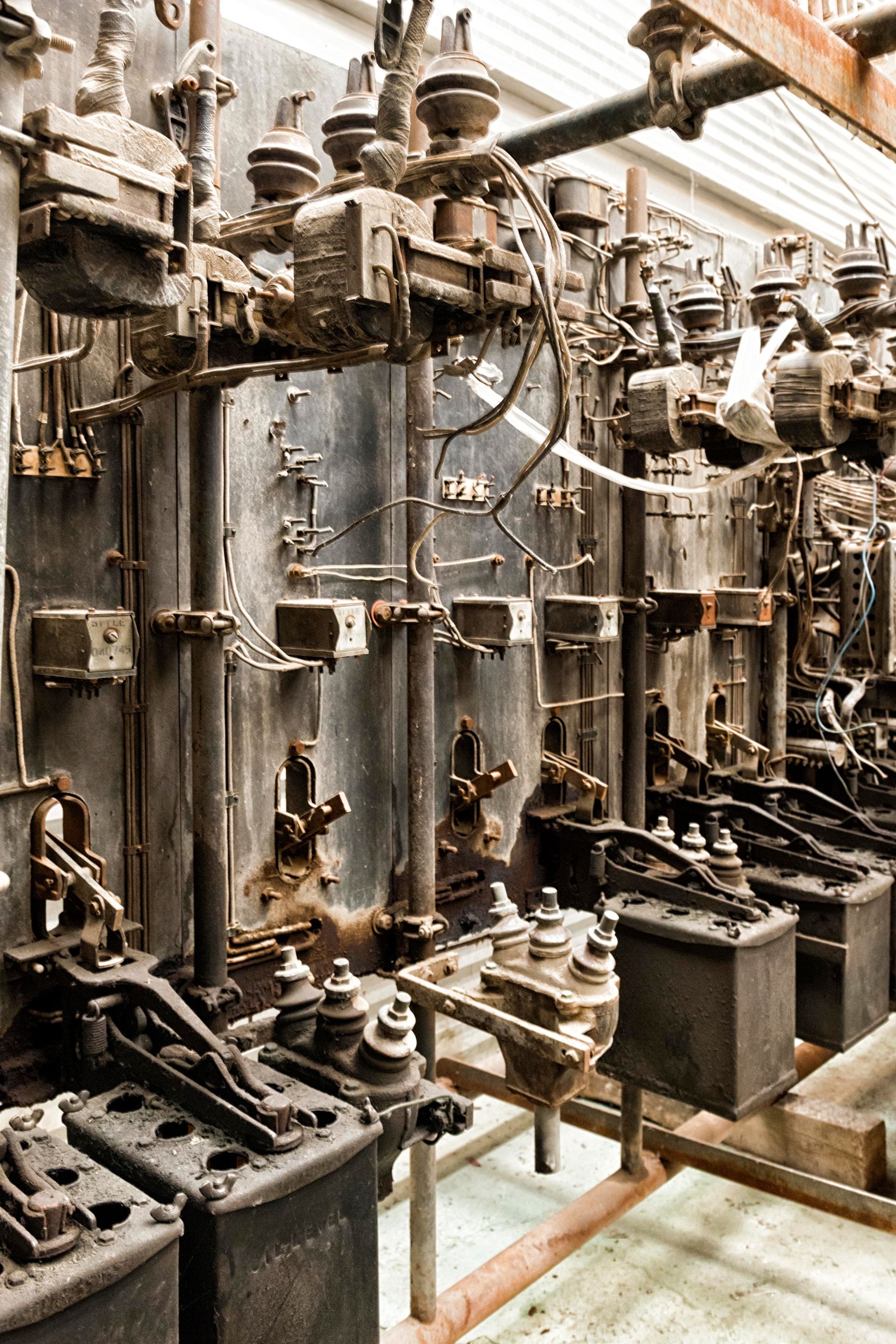 Old, rusted industrial electrical equipment in a dimly lit, possibly abandoned space.