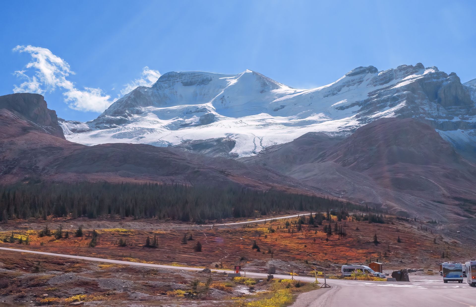 Snowy mountain range with brown and orange fall foliage, clear blue sky.