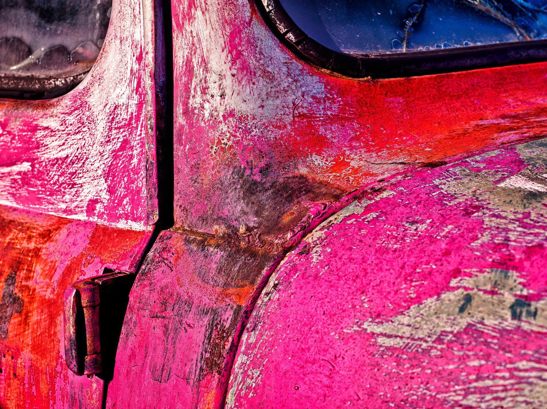 Close-up of peeling red and pink paint on the side of a vehicle.
