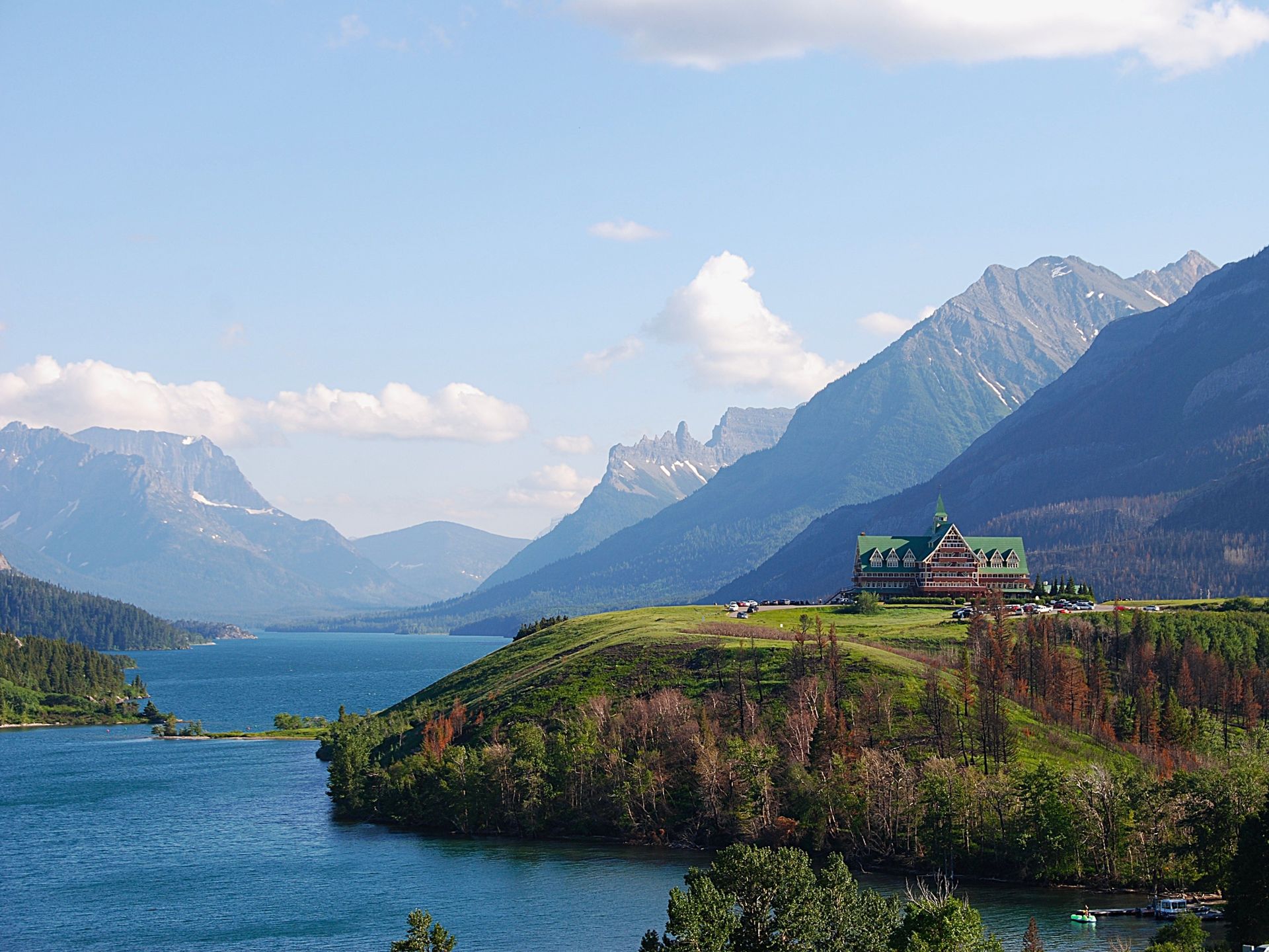 Scenic view of a lake with mountains, a building on a hill, and a blue sky.