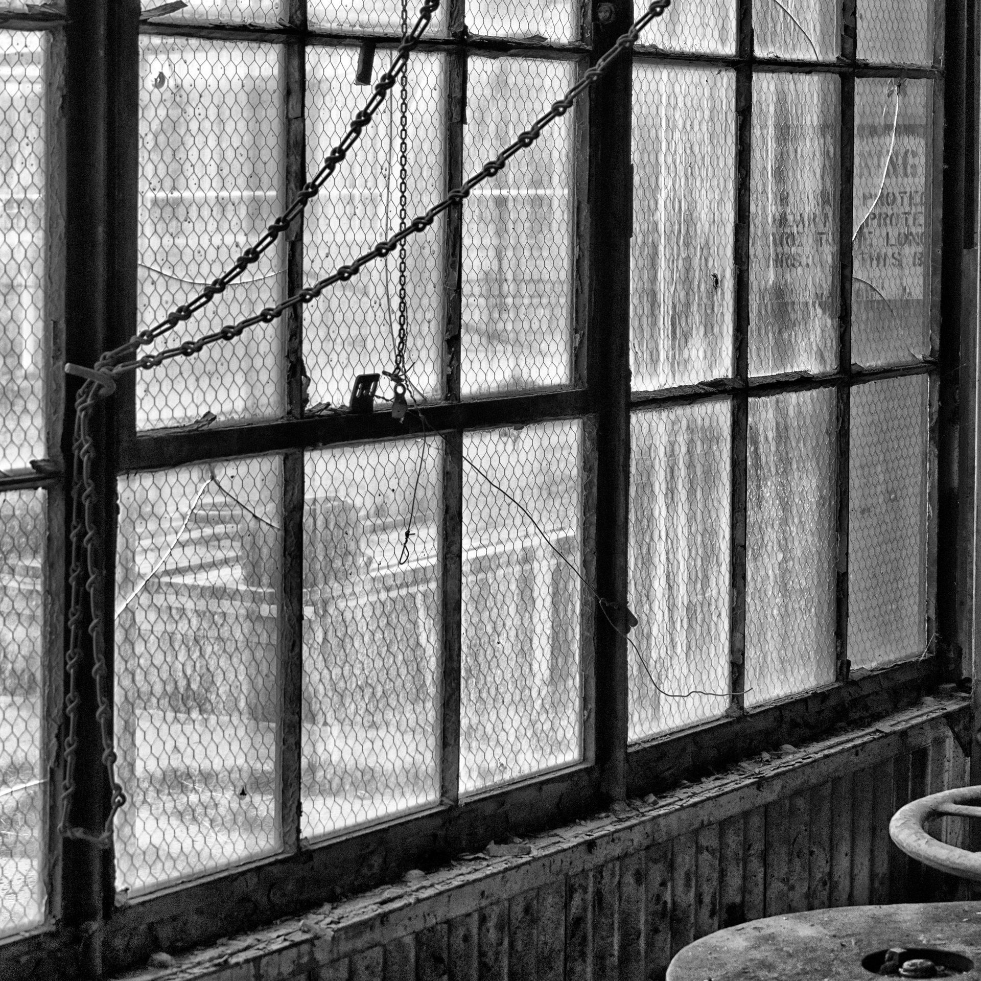Grayscale view of old, broken windows in an industrial building; chain hangs over them.
