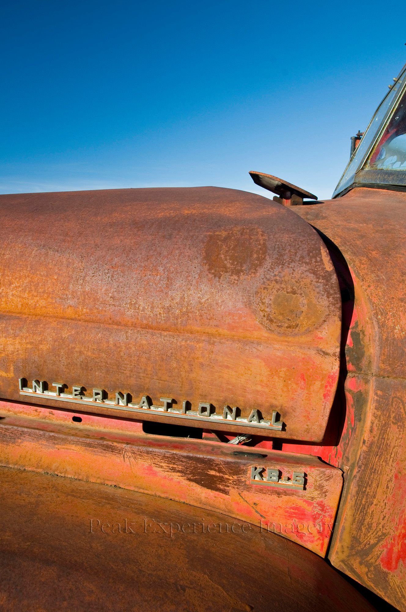 Rusty red International KB-1 truck hood against a bright blue sky.