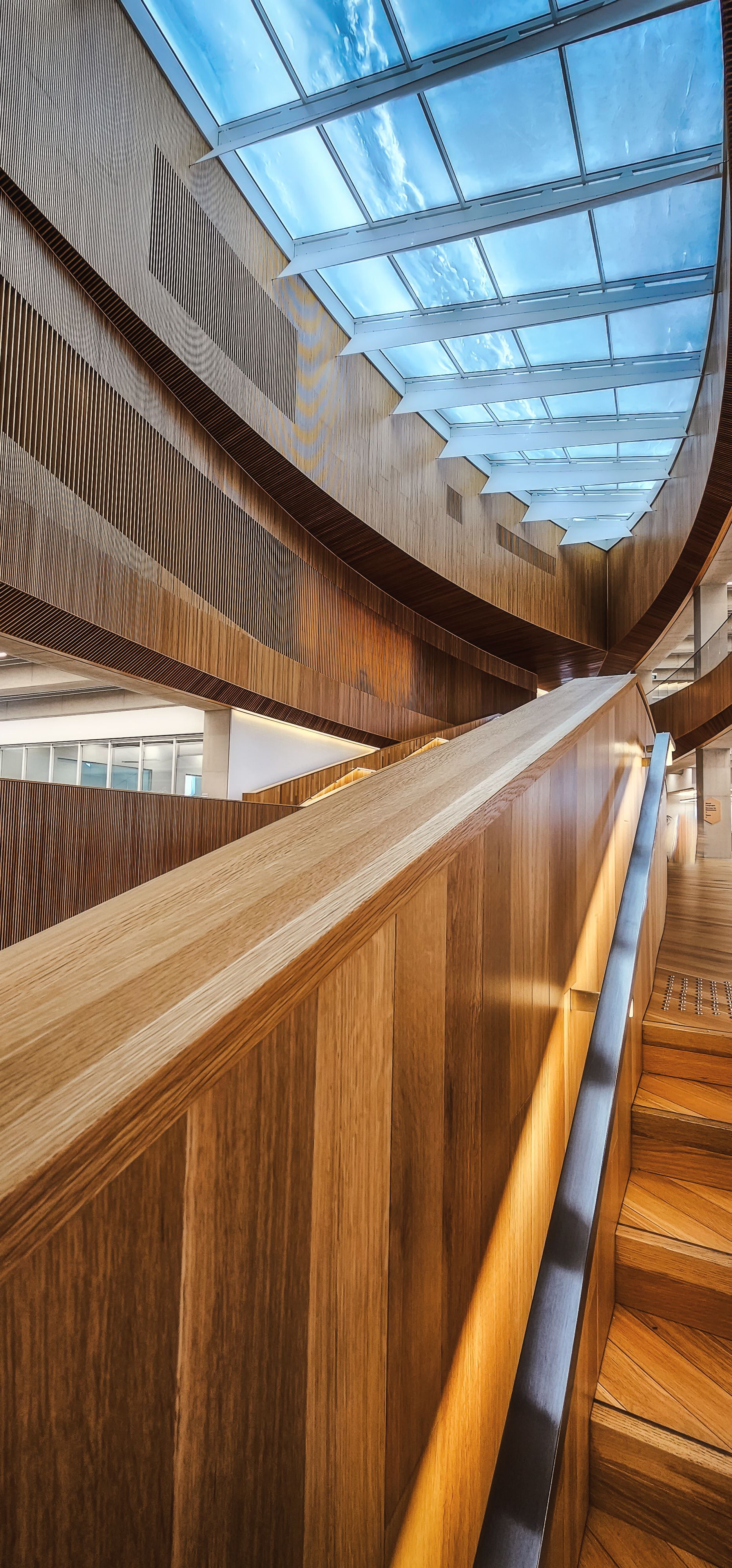 Wooden staircase with a handrail, leading up toward a skylight.