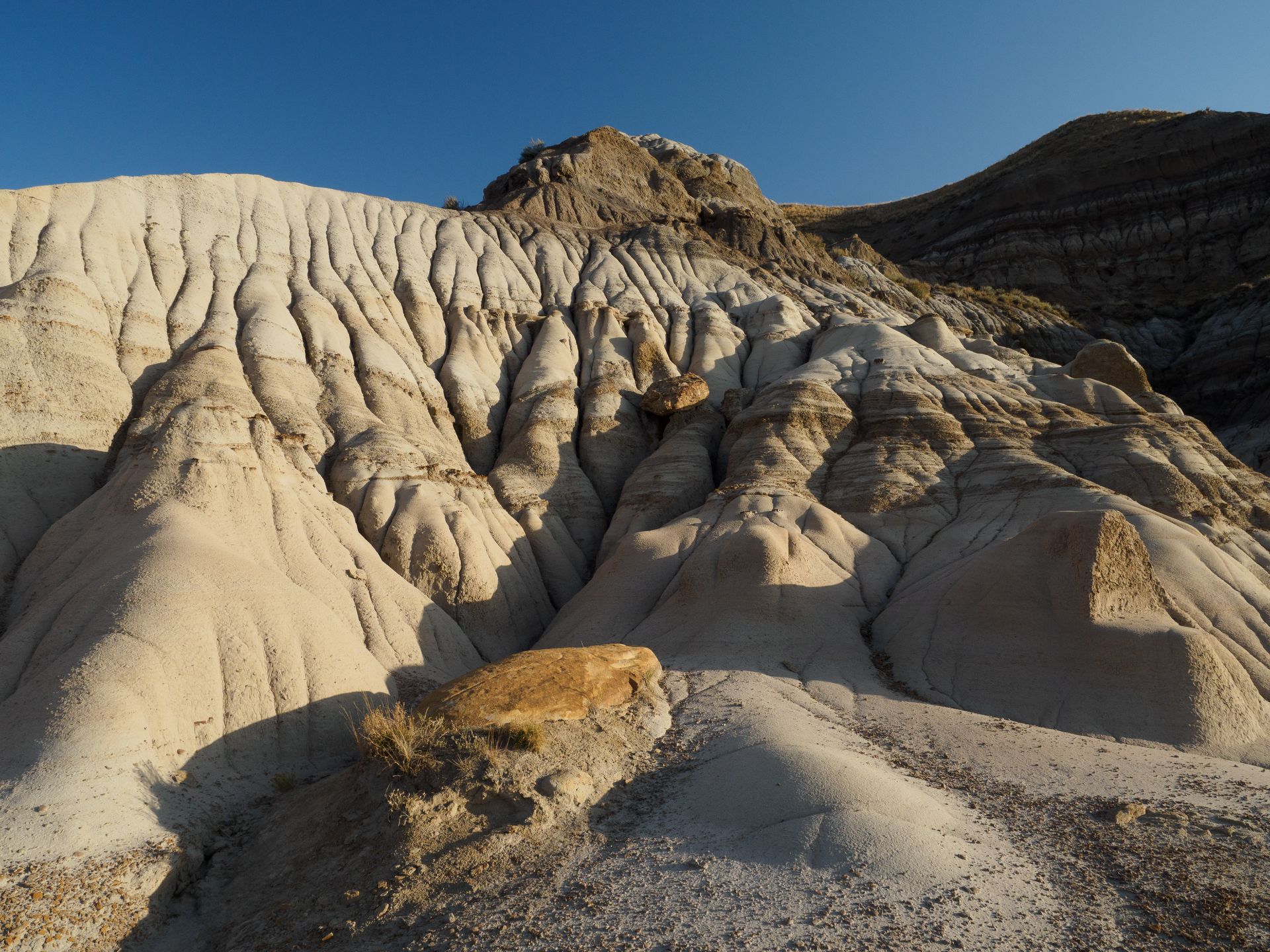Eroded badlands landscape with light-colored, textured rock formations under a blue sky.