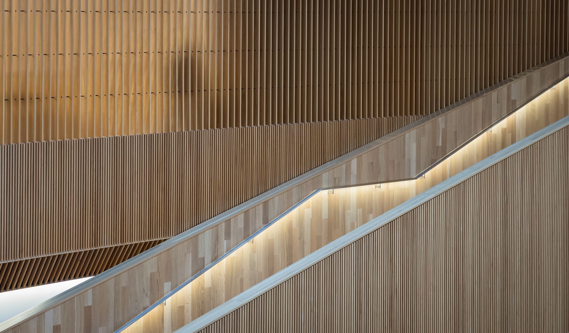 Wooden staircase with vertical slat walls and illuminated handrail.