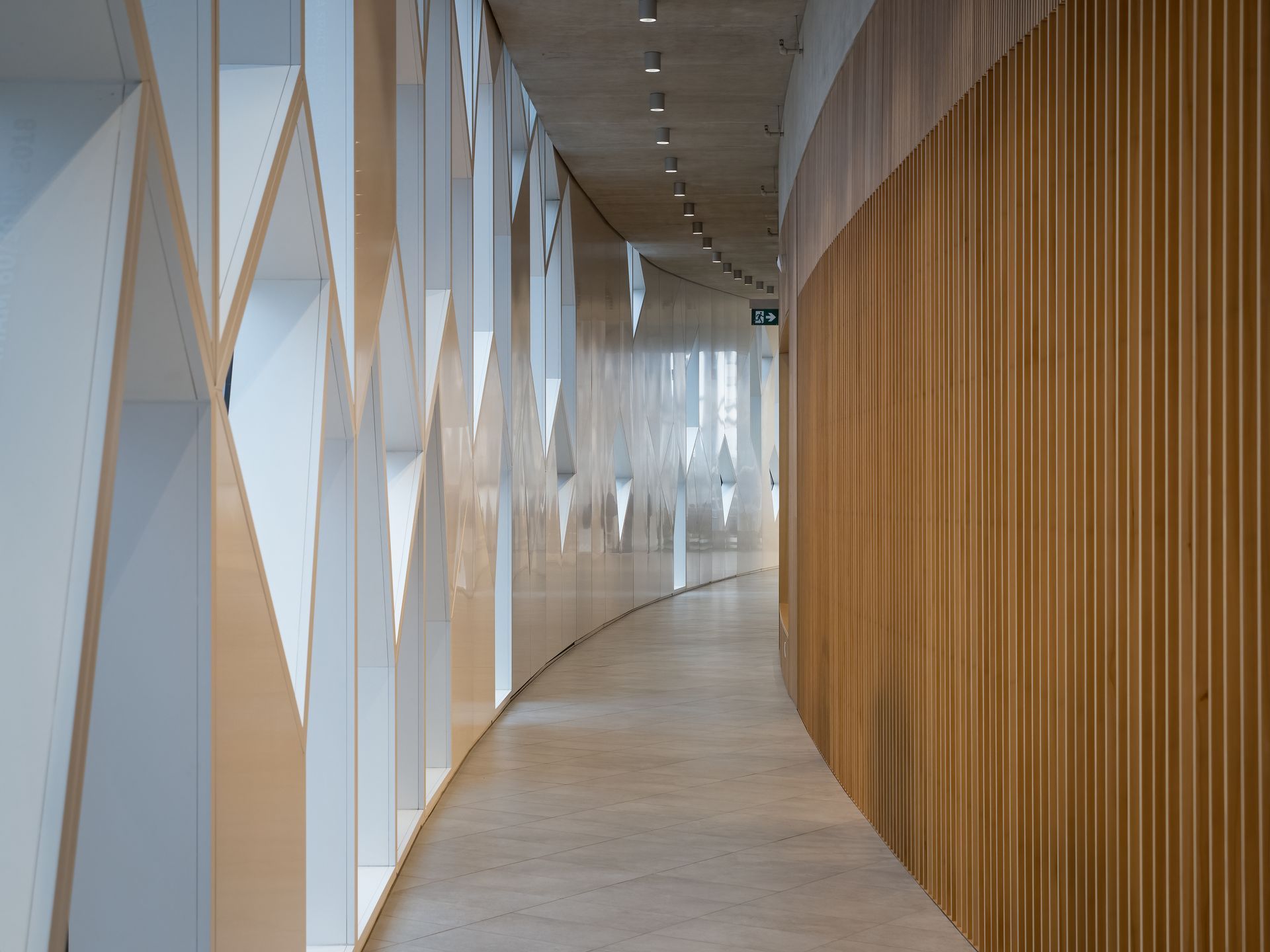 Curving hallway with wooden panel wall, geometric white wall, and concrete floor.