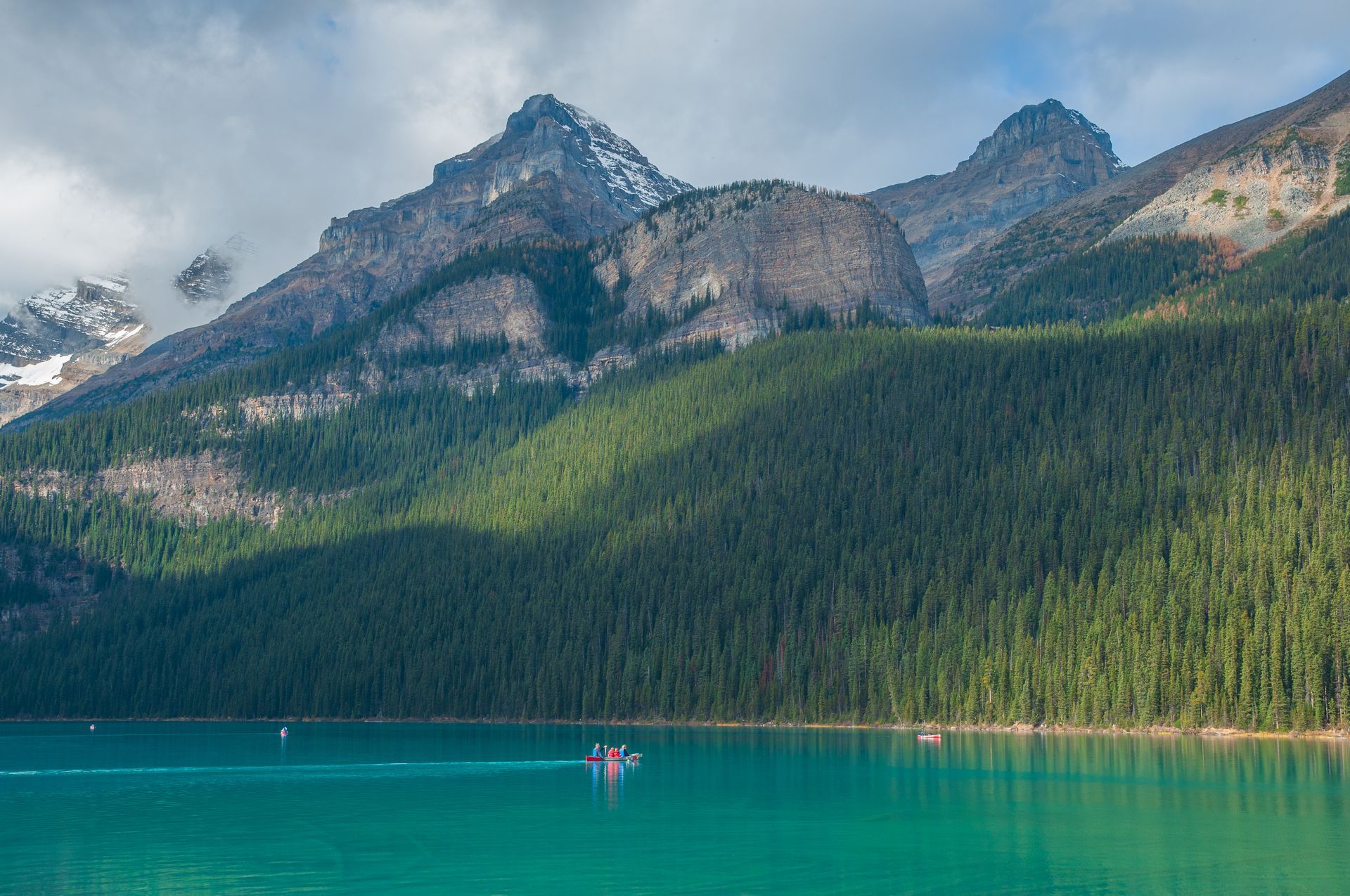 Turquoise lake in front of a forest and mountain range; sunlight and shadows.