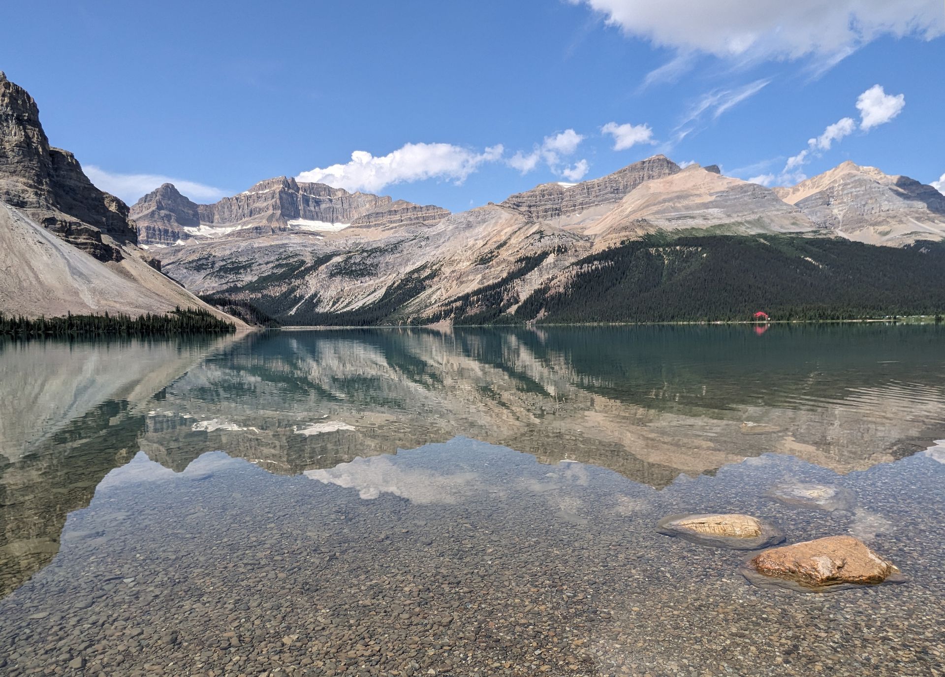Mountains and blue sky reflected in a clear, still lake. Brown rocks in foreground.