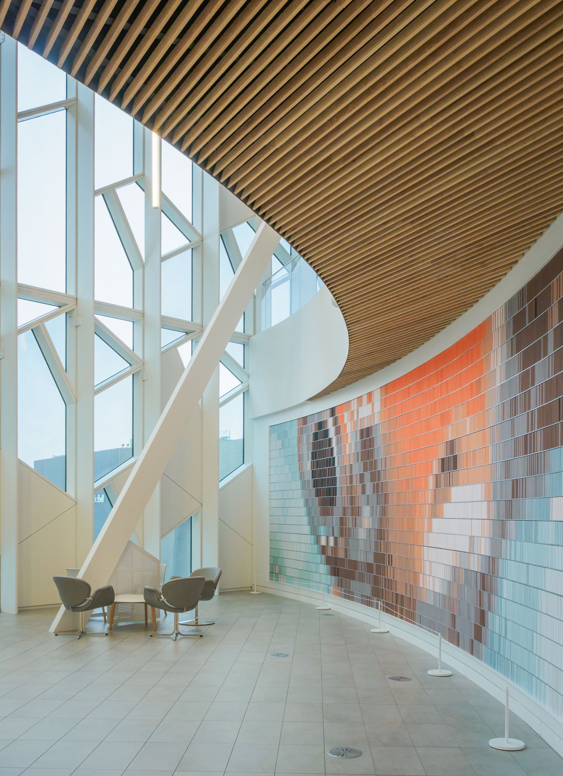 Modern interior with curved wall art, high windows, wood ceiling, chairs.