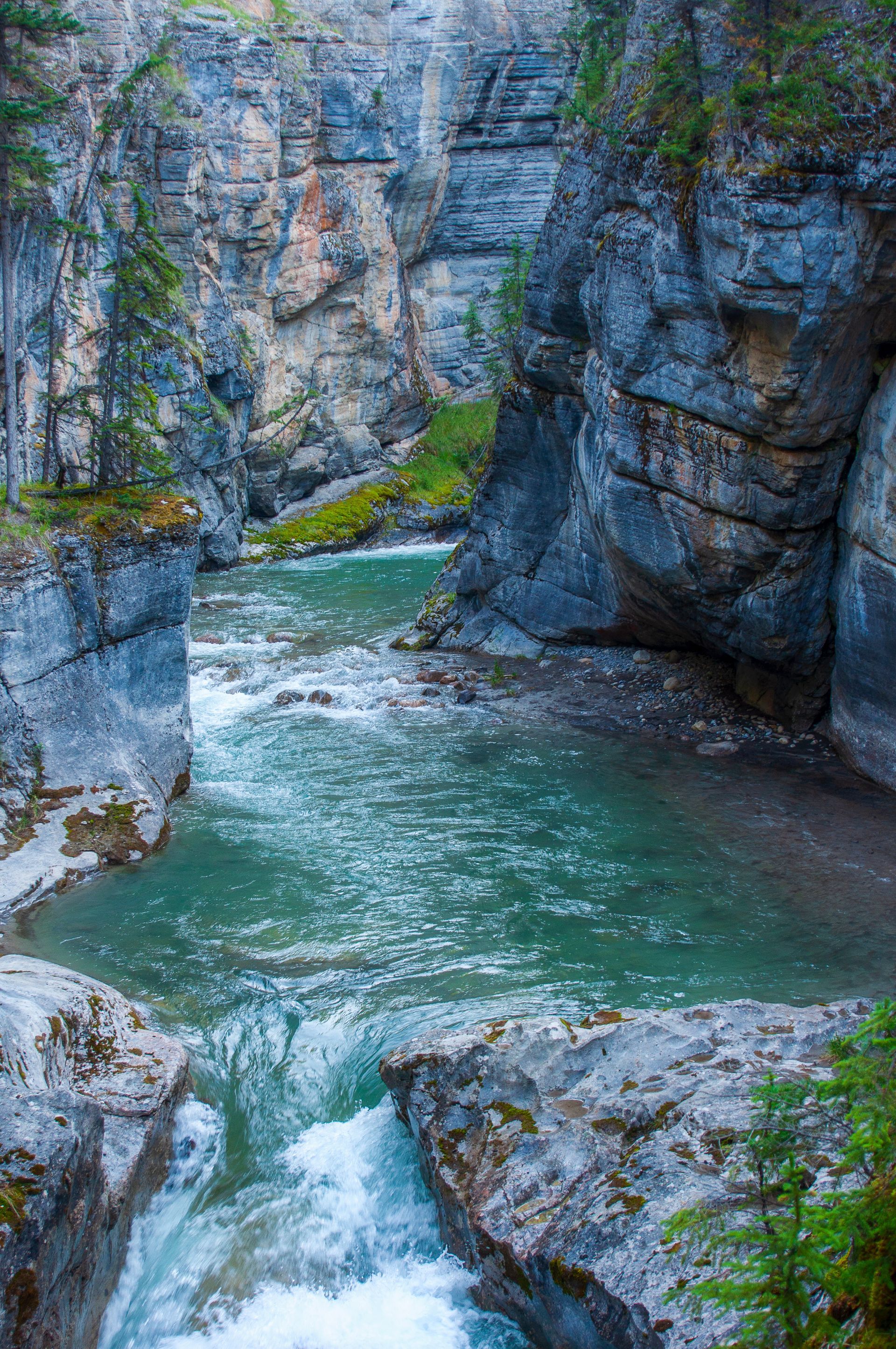 Canyon with turquoise river flowing through rocky walls, with green vegetation.