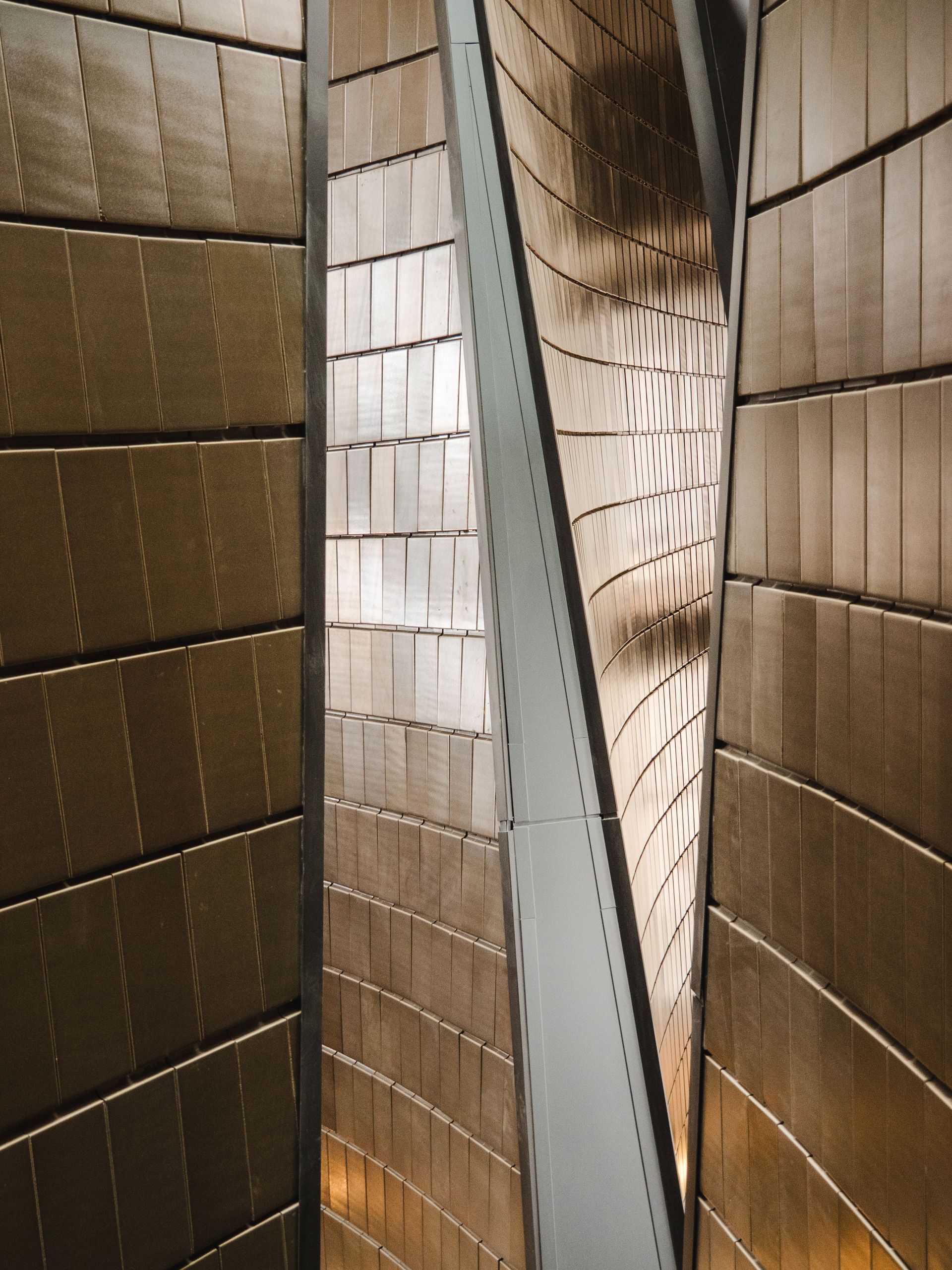 Abstract shot of bronze-colored tiled walls twisting around a central metallic column.