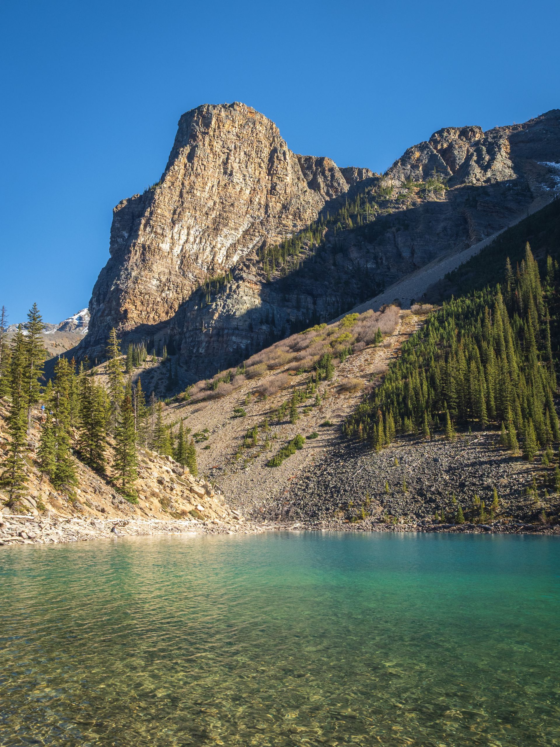 Crystal-clear turquoise lake with a rocky mountain backdrop under a bright blue sky.