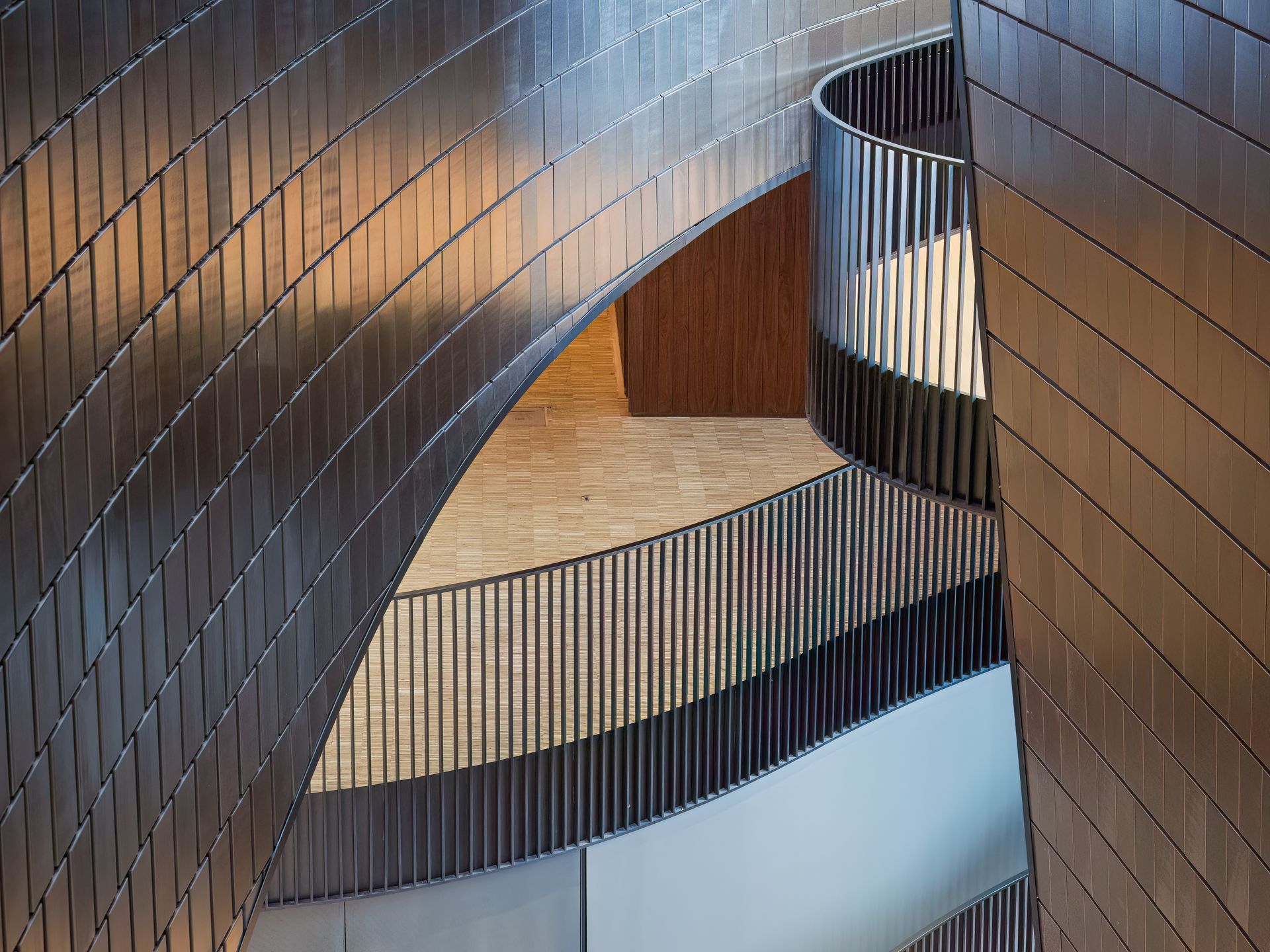 Curving metallic wall with a spiraling staircase and railing.