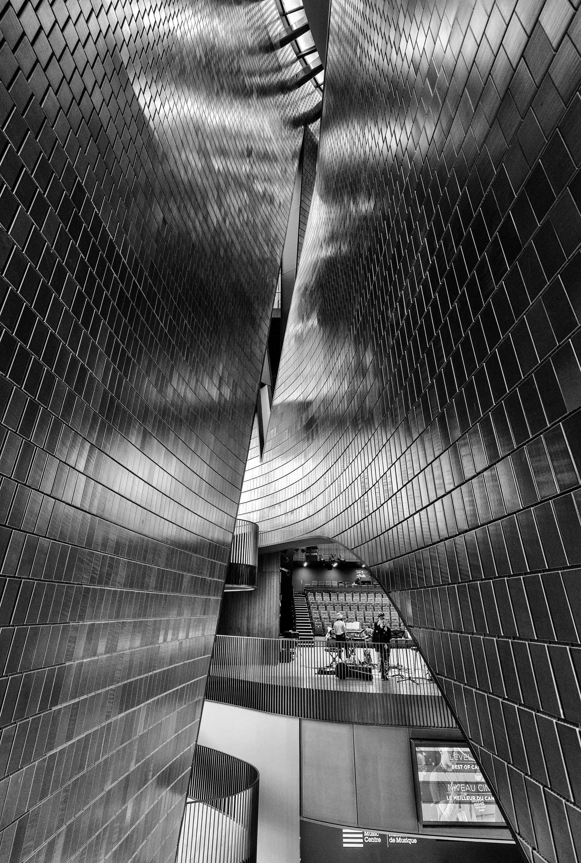 Black and white photo of a modern building interior with a corridor of textured metal walls leading to a distant view.
