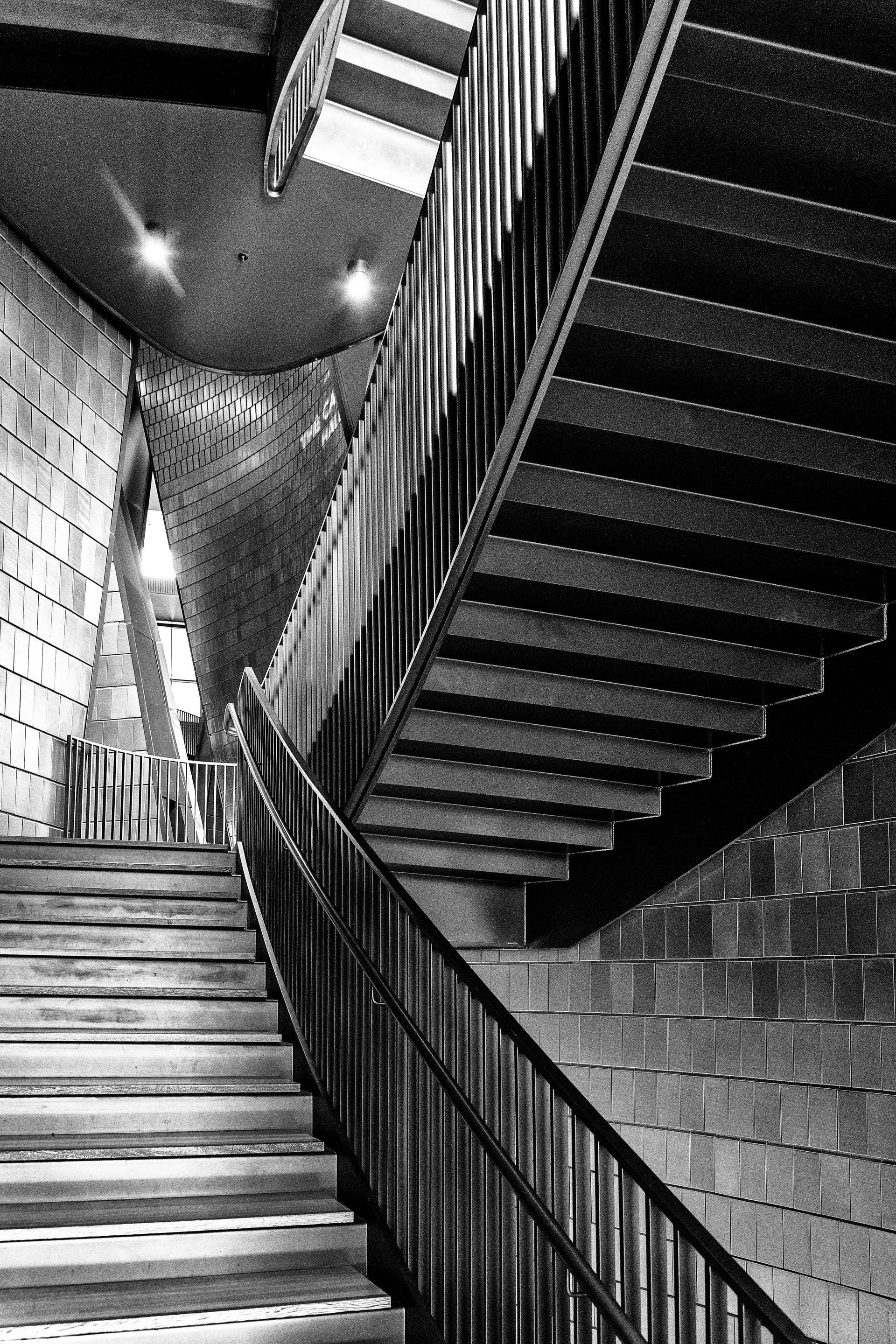 Black and white photo of a staircase with brick walls and dark railings.