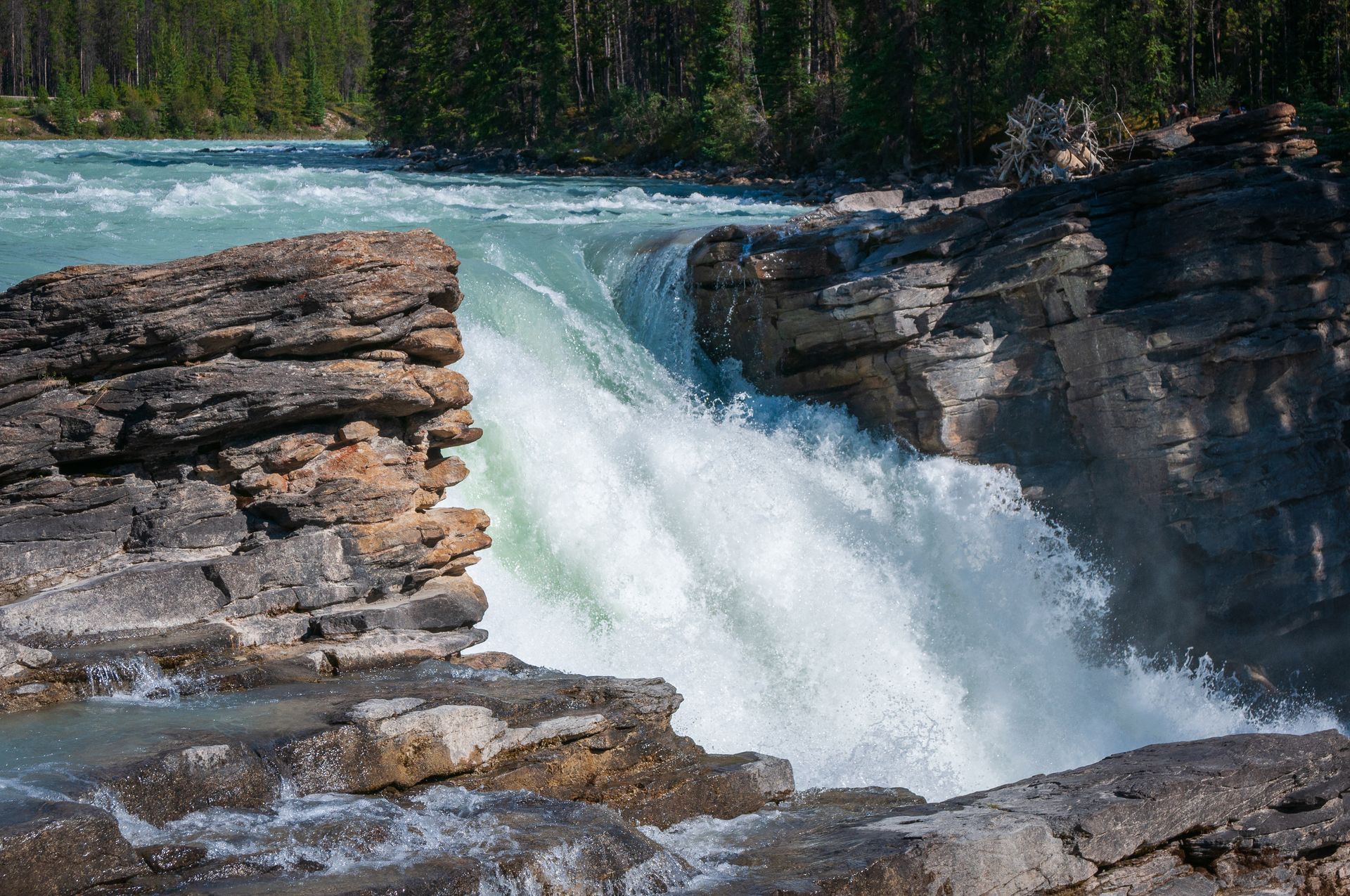 Waterfall cascading through rock formation, turquoise water. Forest in background.