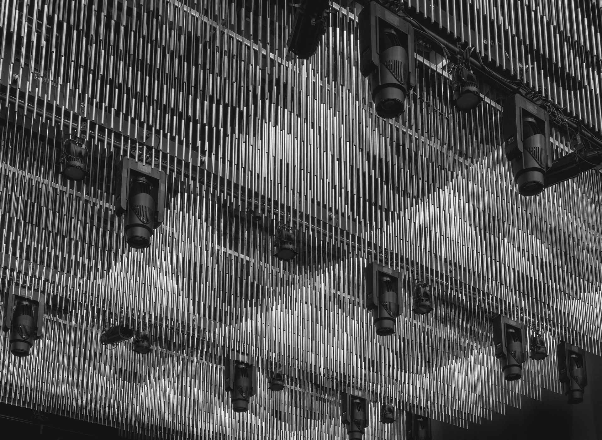 Black and white photo of a stage ceiling with many hanging vertical rods and spotlights.