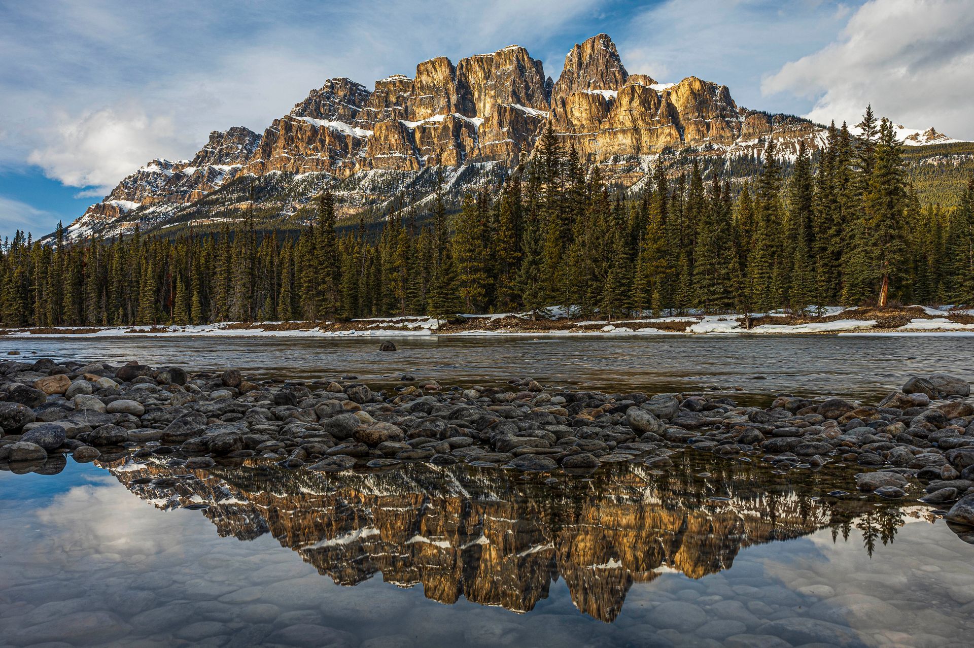 Rocky mountain range reflected in calm water. Forest in front.