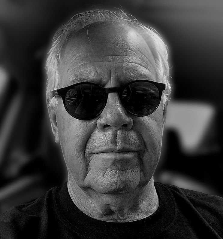 Man with glasses, bald head, and plaid shirt smiling.