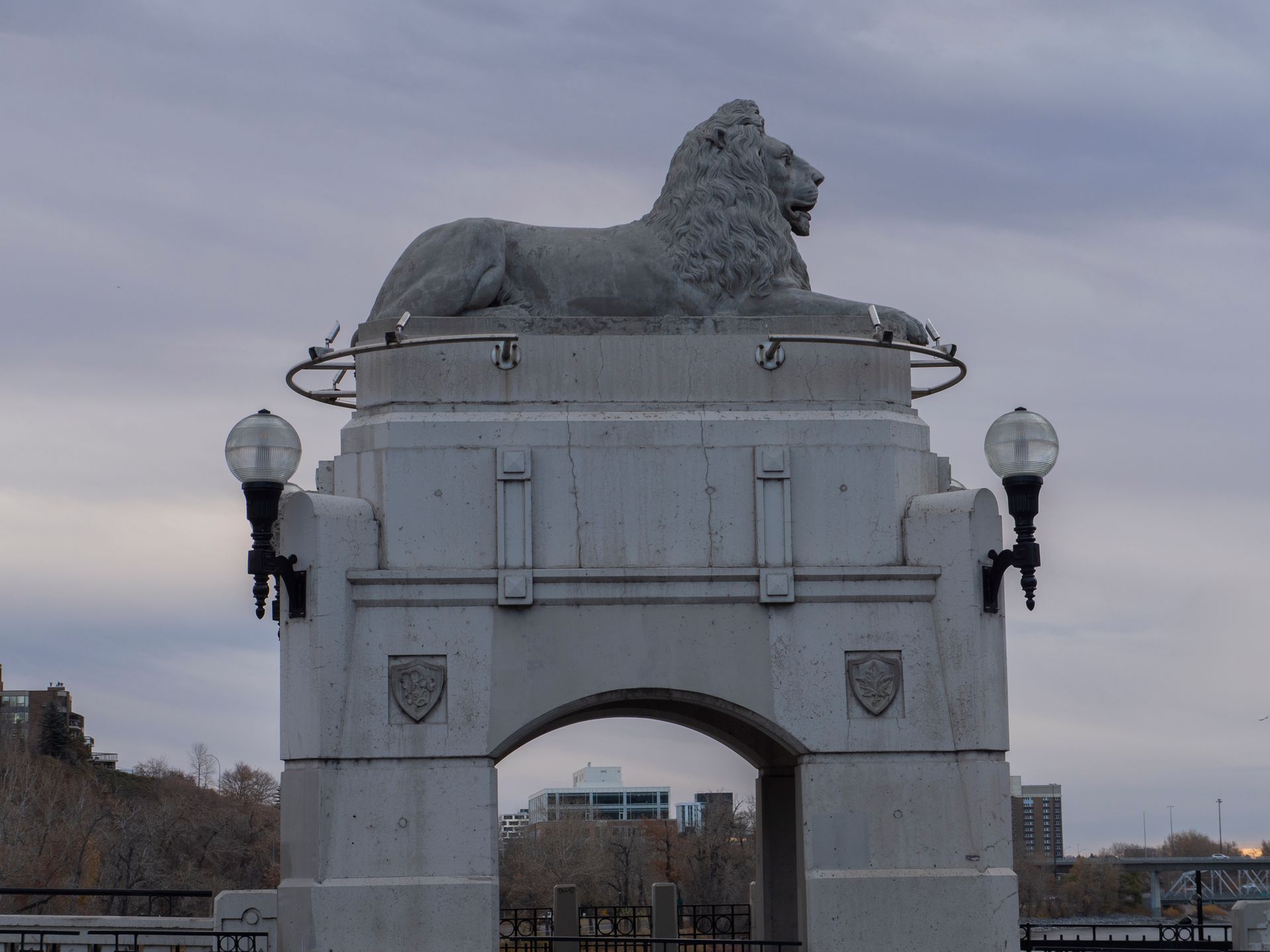 Stone lion statue atop archway with streetlights, overcast sky.