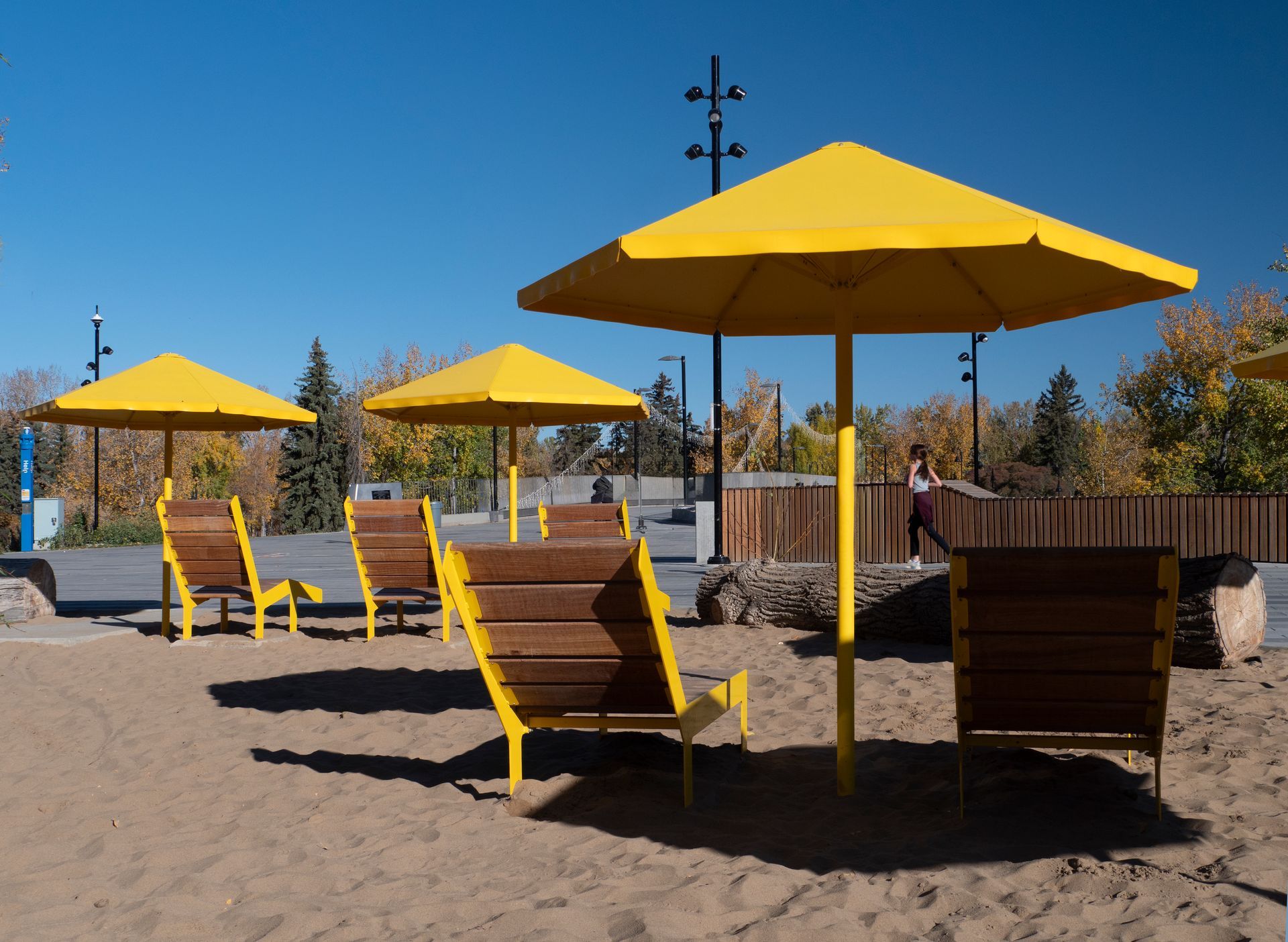 Yellow umbrellas and lounge chairs on a sandy area; person walking in the background.