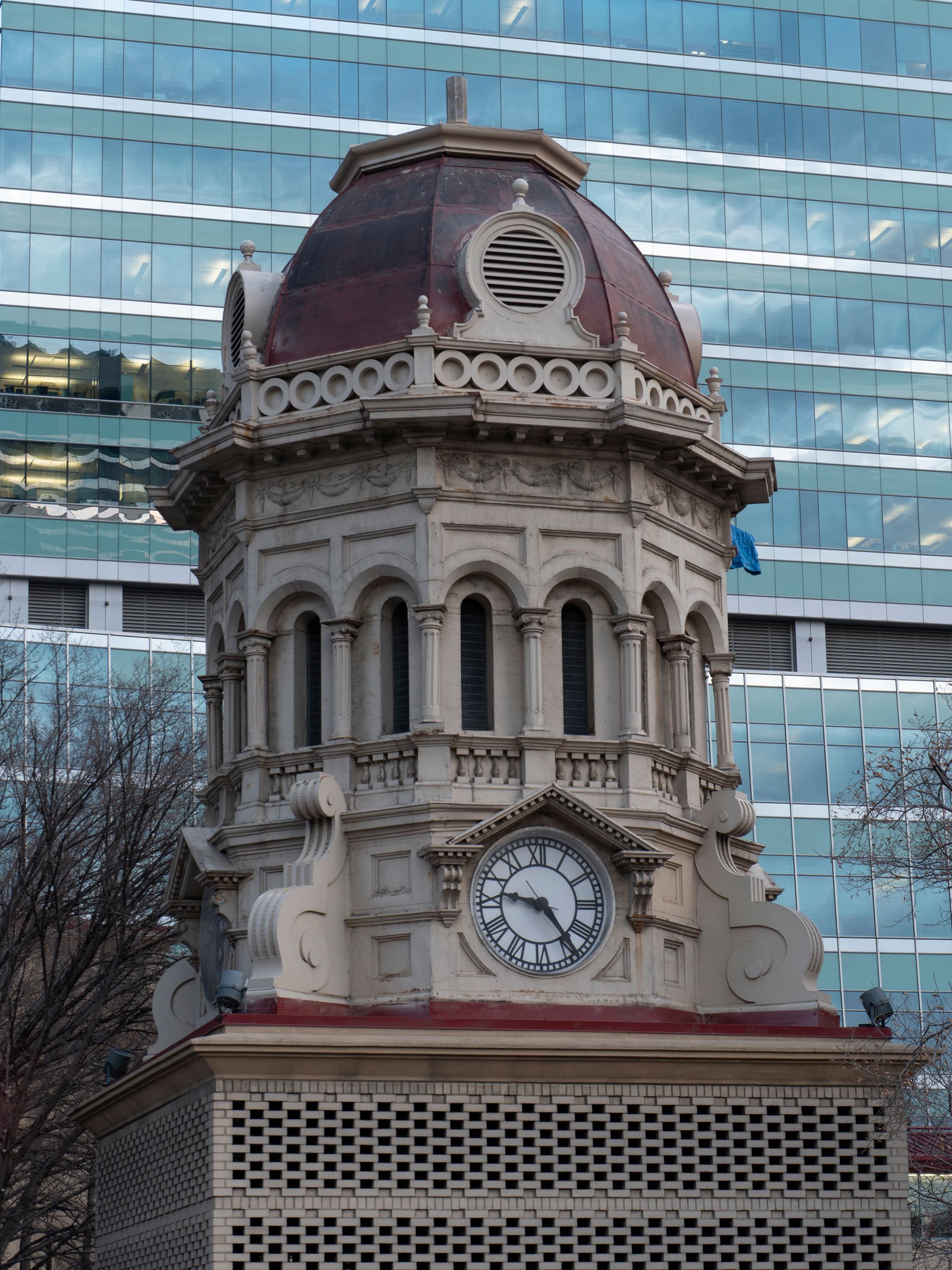 Clock tower with ornate detailing, a maroon dome, and a modern glass building background.