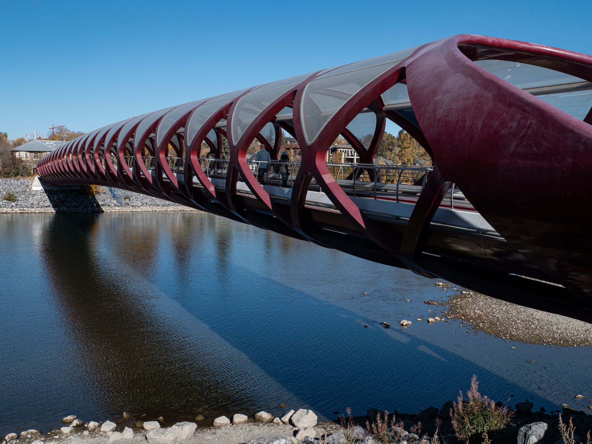 Red pedestrian bridge over river, with unique, arching design. Sunny day.