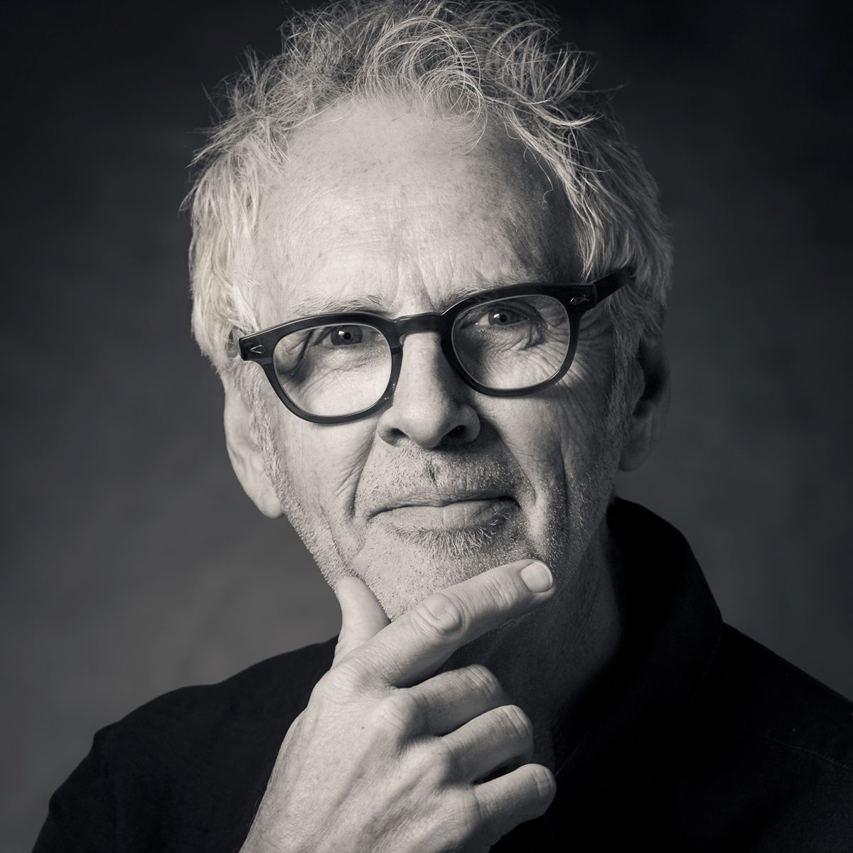 Man wearing glasses, holding his chin, thoughtful expression.