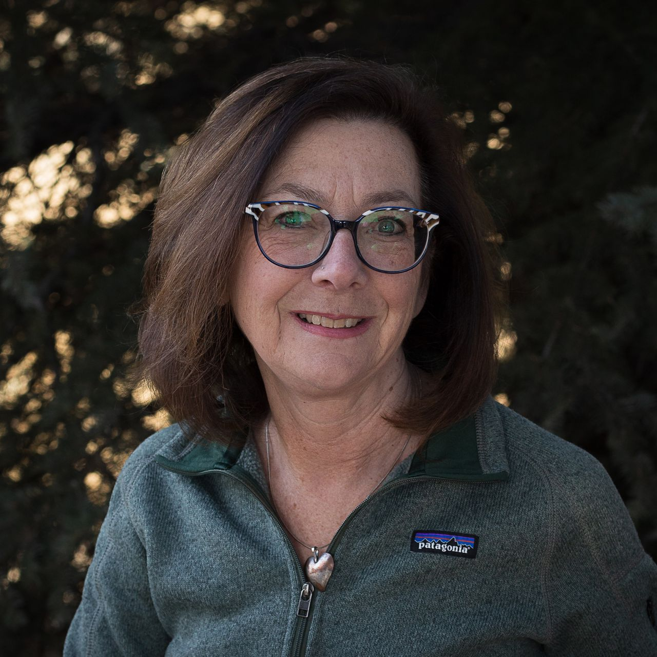 Man in blue jacket adjusts gloves outdoors, snow-covered rocks in the background. Camera around his neck.