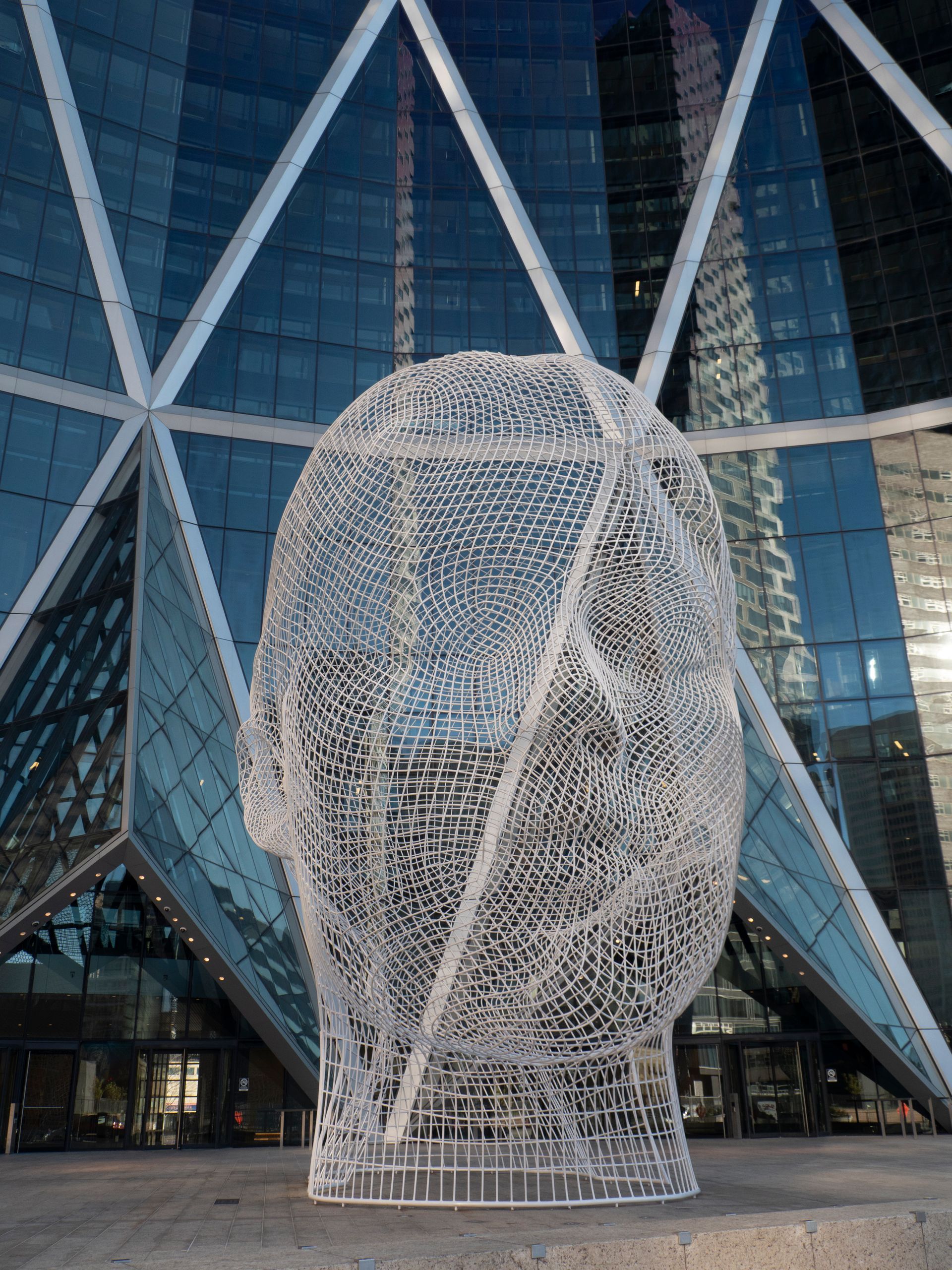 A large, wire sculpture of a head in front of a modern glass building.