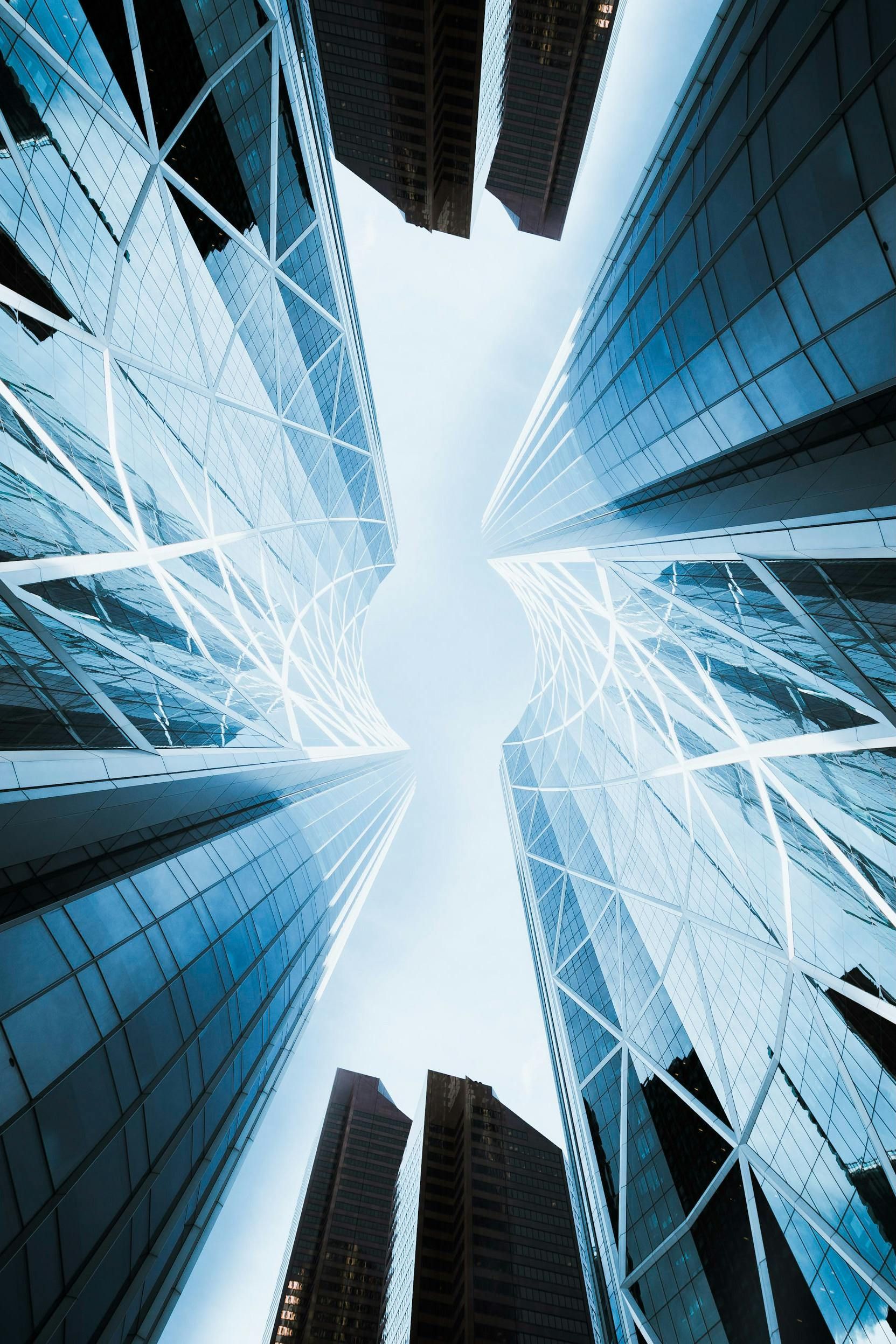 Low-angle shot of tall, modern skyscrapers with blue-tinted glass against a light blue sky.
