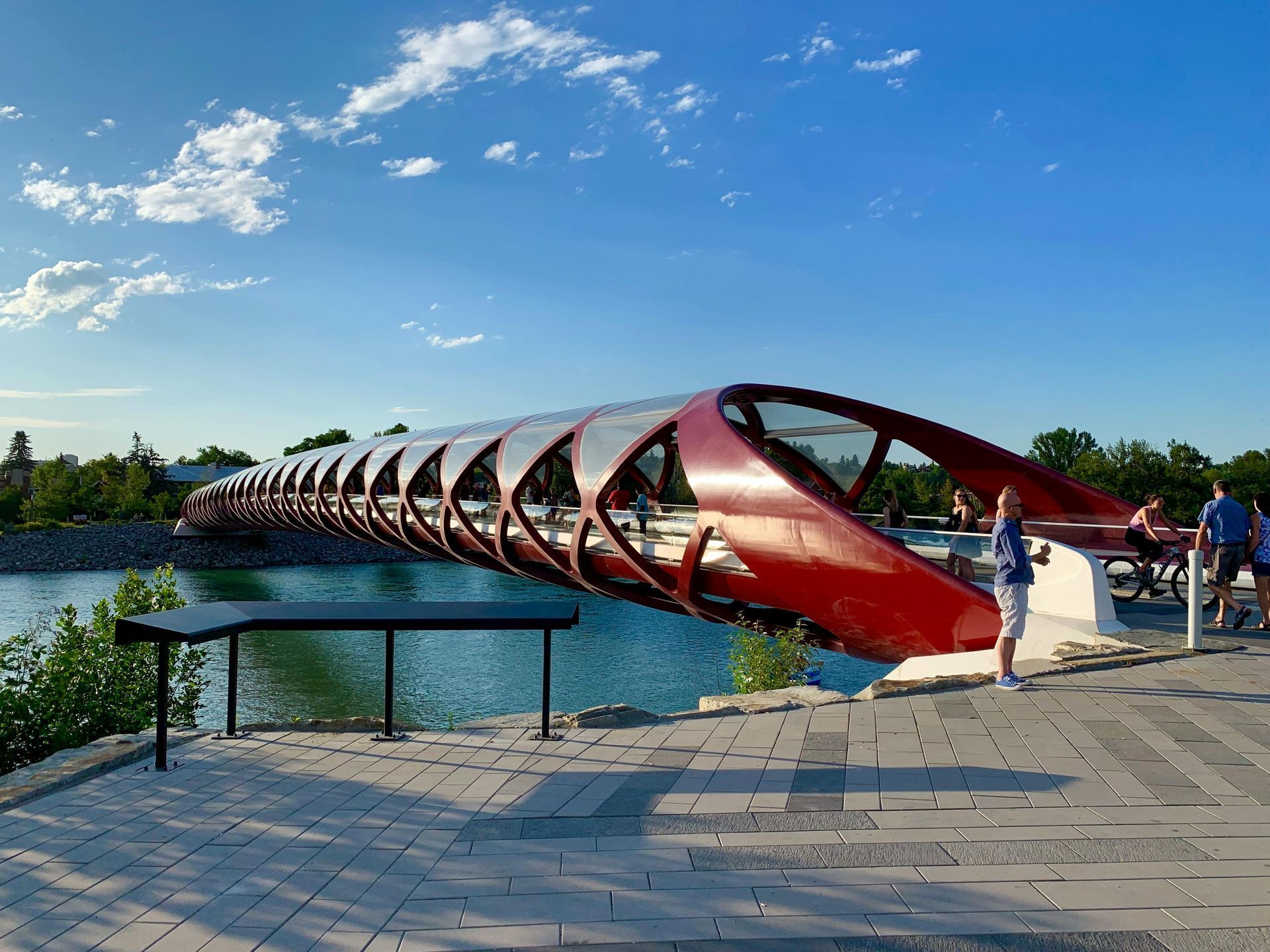 Red Peace Bridge over water, blue sky. People walking on the bridge, paved walkway.