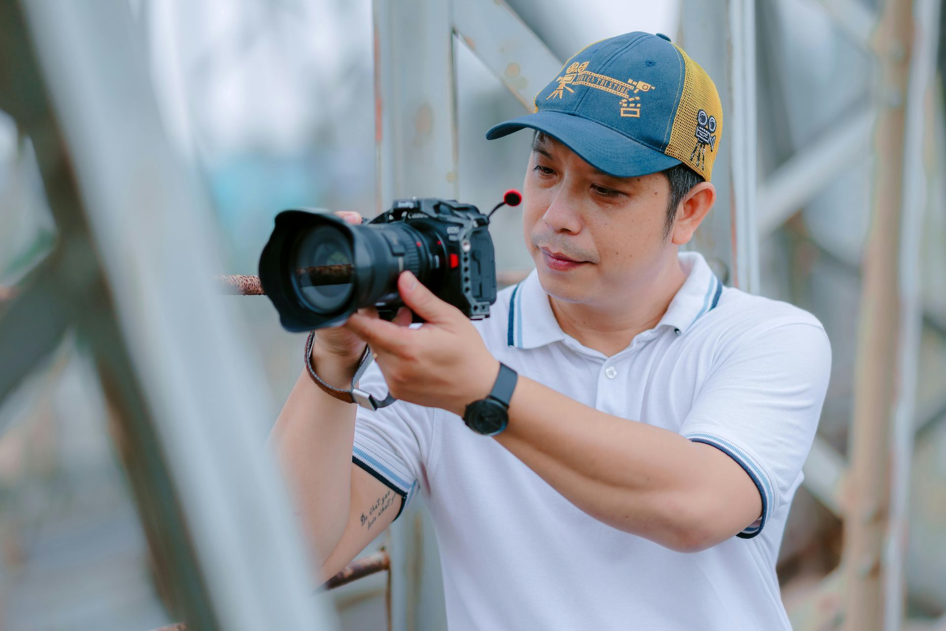 Man holding a camera, focused, wearing a blue hat and white shirt, outdoors.