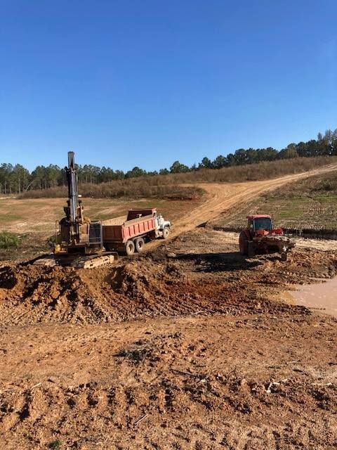 Construction site with an excavator, dump truck, and compactor working on dirt road under a blue sky.