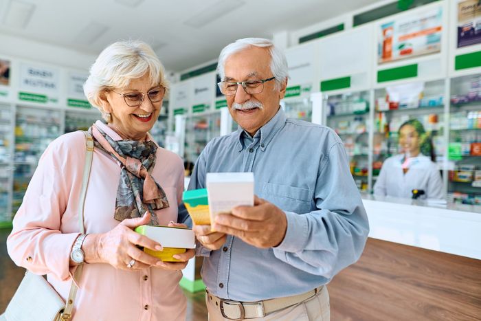 An elderly couple is looking at a box of pills in a pharmacy.