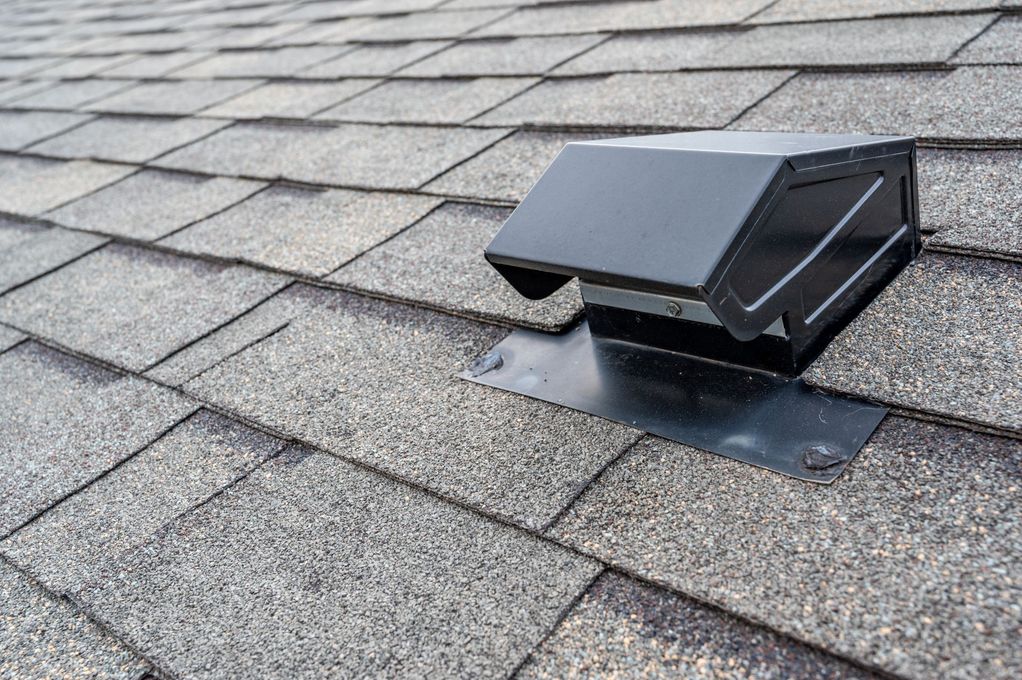 Black vent on a gray shingle roof, angled view.