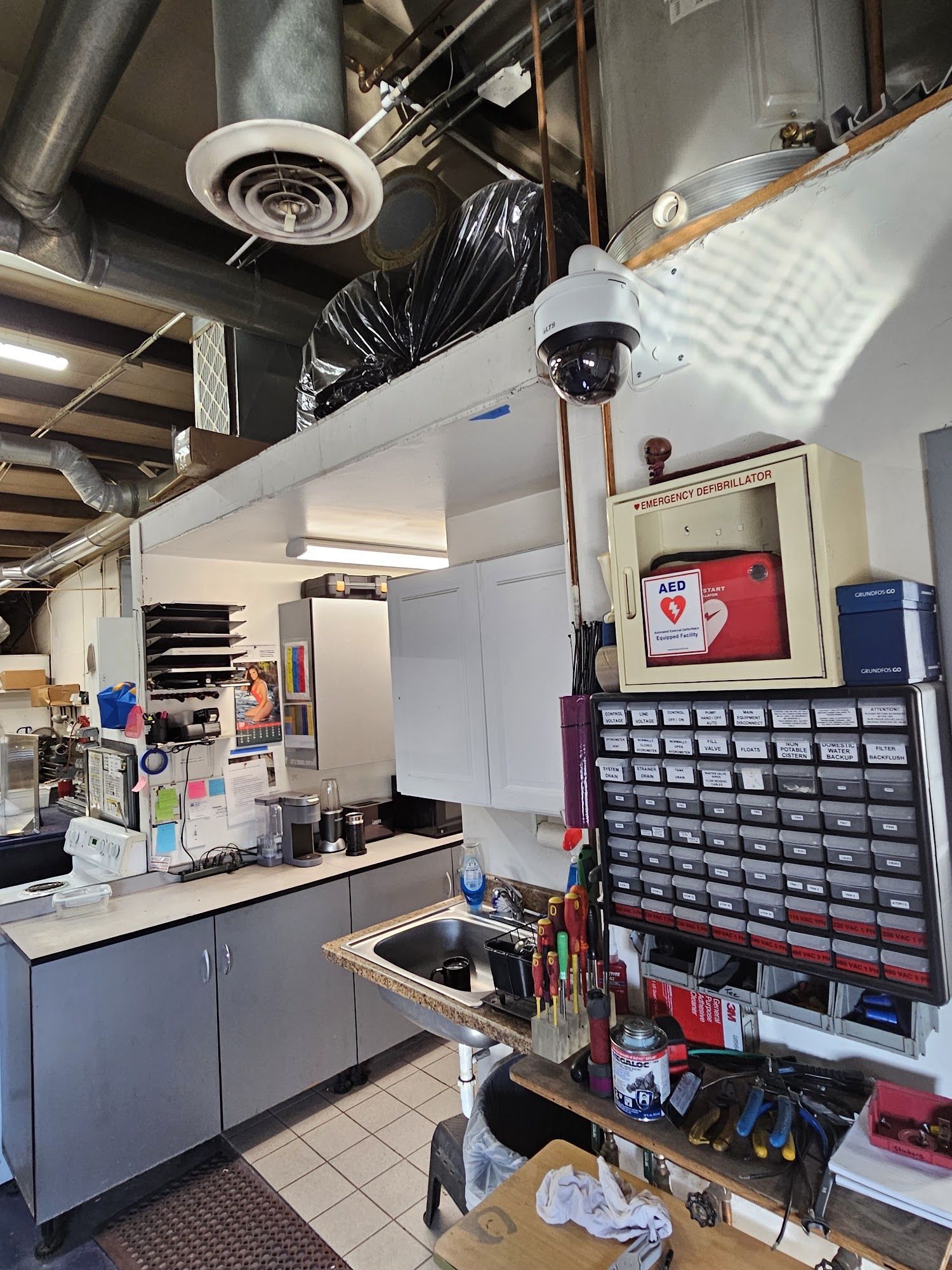 A cluttered workshop interior with cabinets, tools, and a security camera mounted overhead.