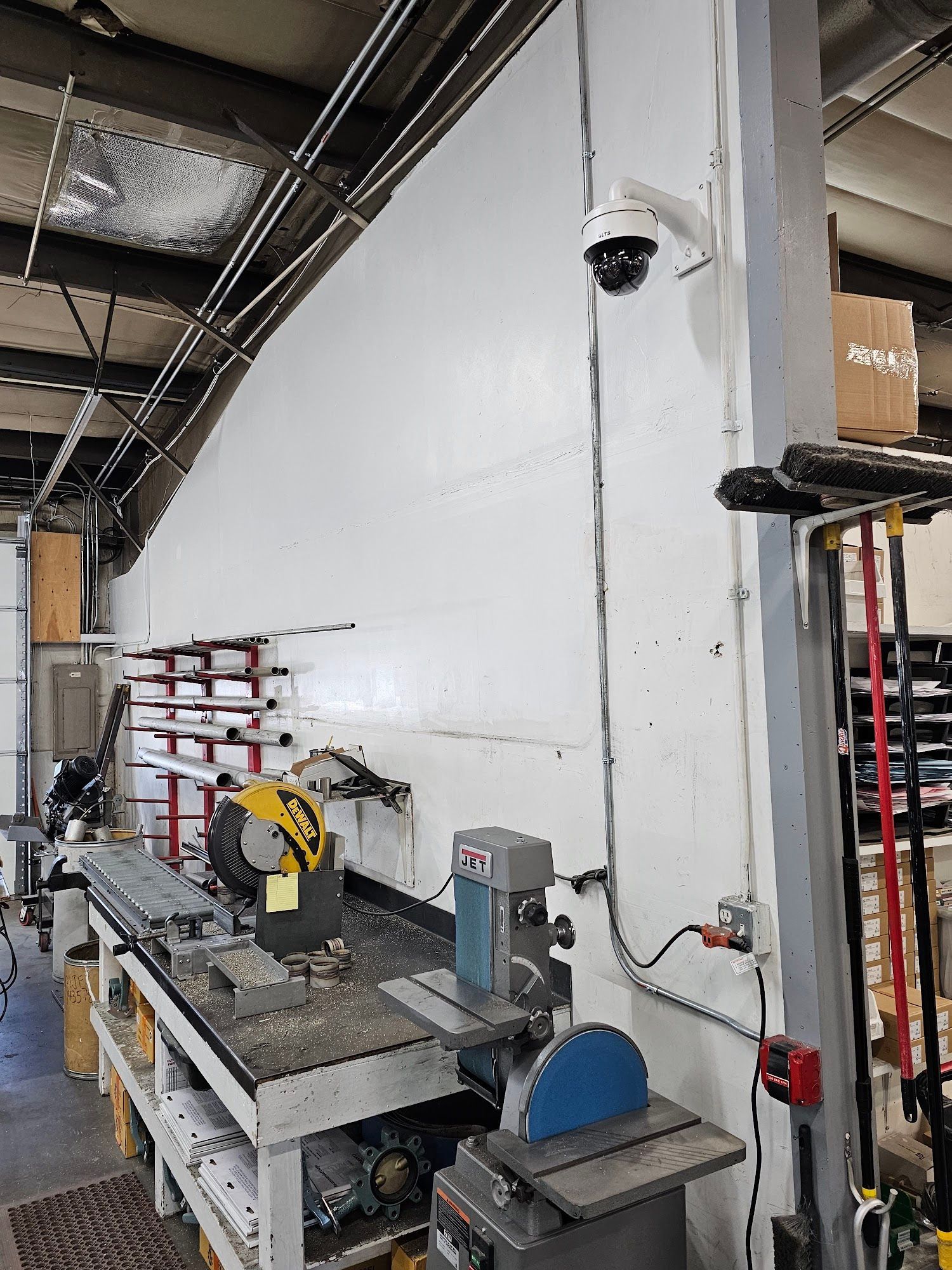 A workshop interior with a white wall, tools, and a security camera mounted on a pillar.