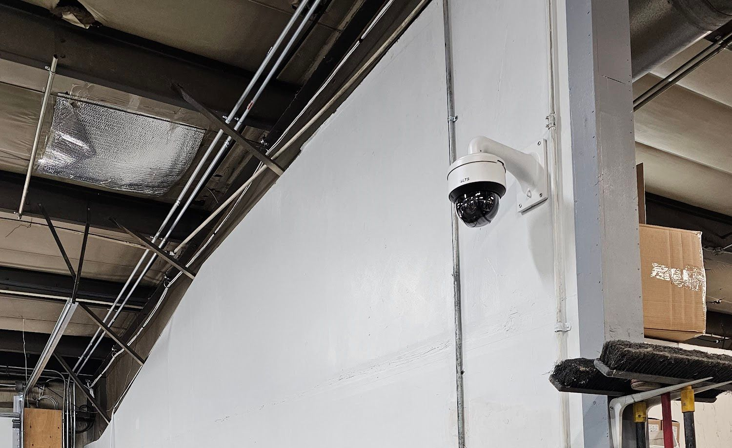 Security camera mounted on a white wall in an industrial setting, angled towards an open space.