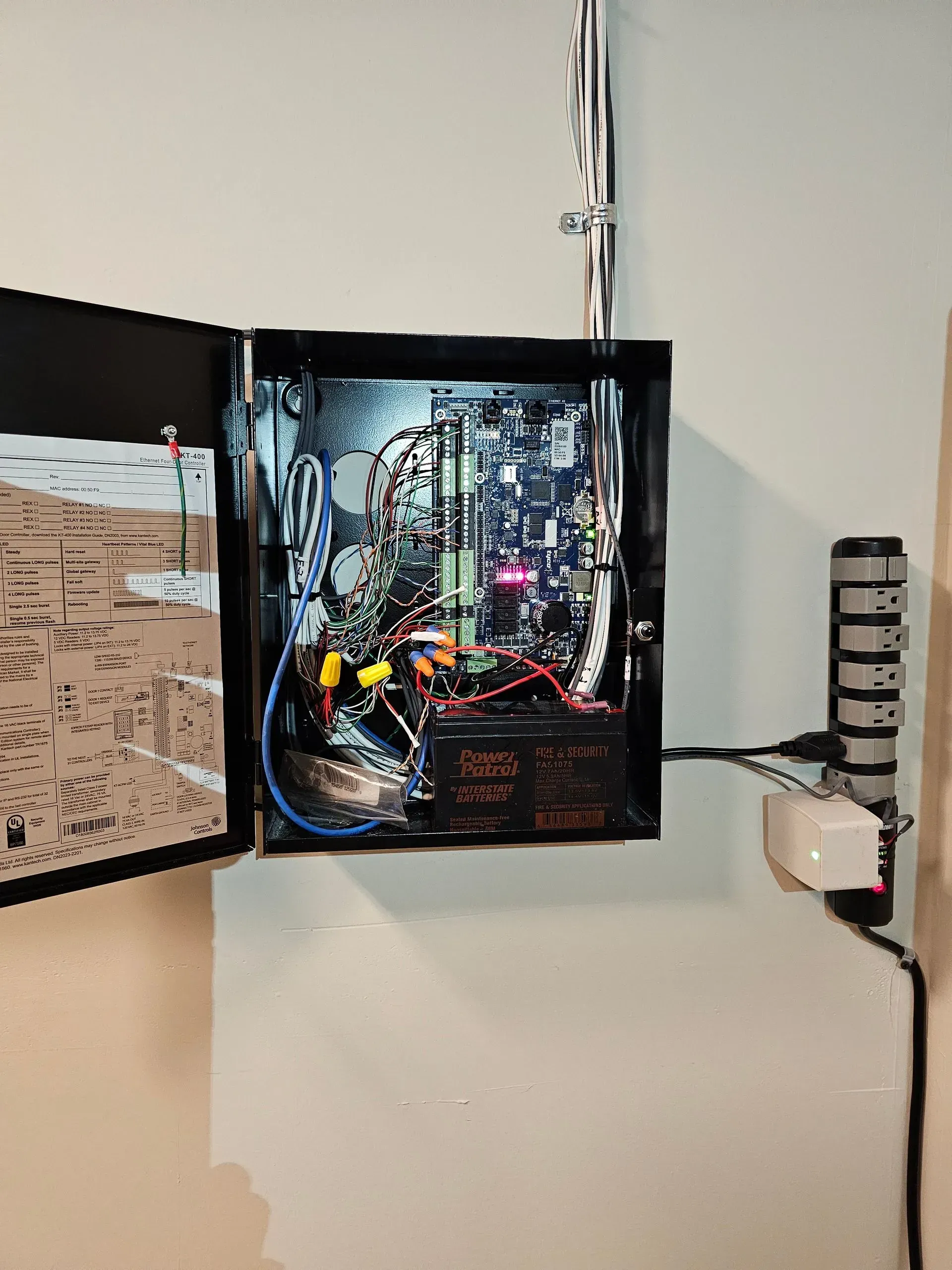 Open electrical box with circuit boards, battery, wires, and power cord.