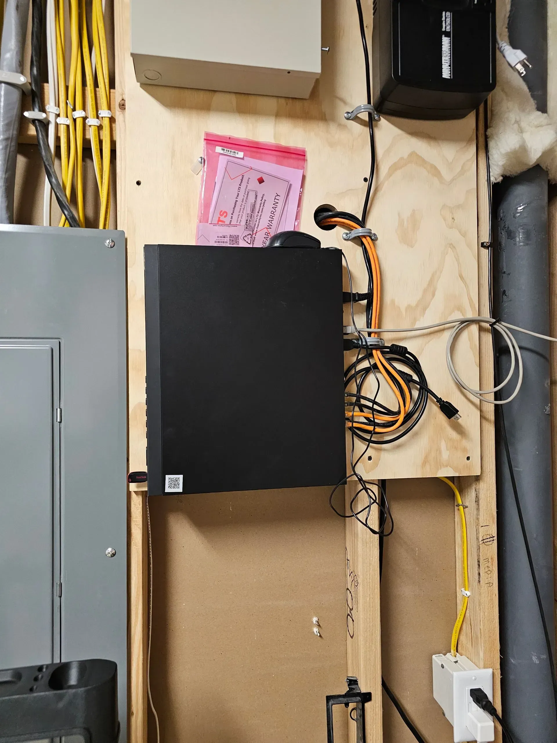 Black security server mounted on a wooden panel, various cables and electrical components surround it.