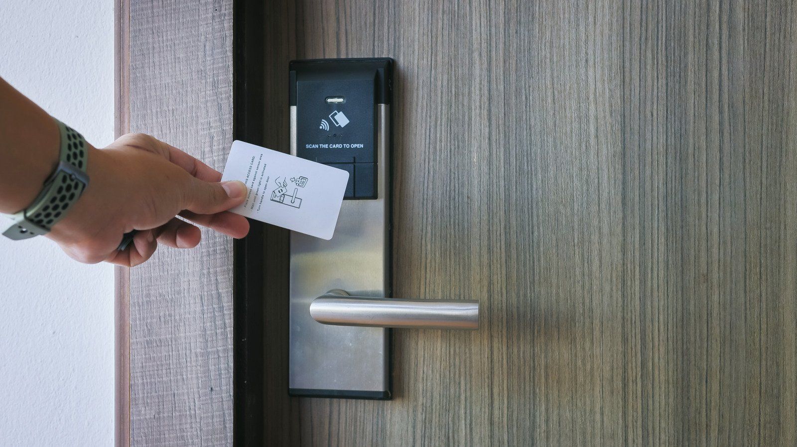 Hand with hotel key card unlocking a wooden door.