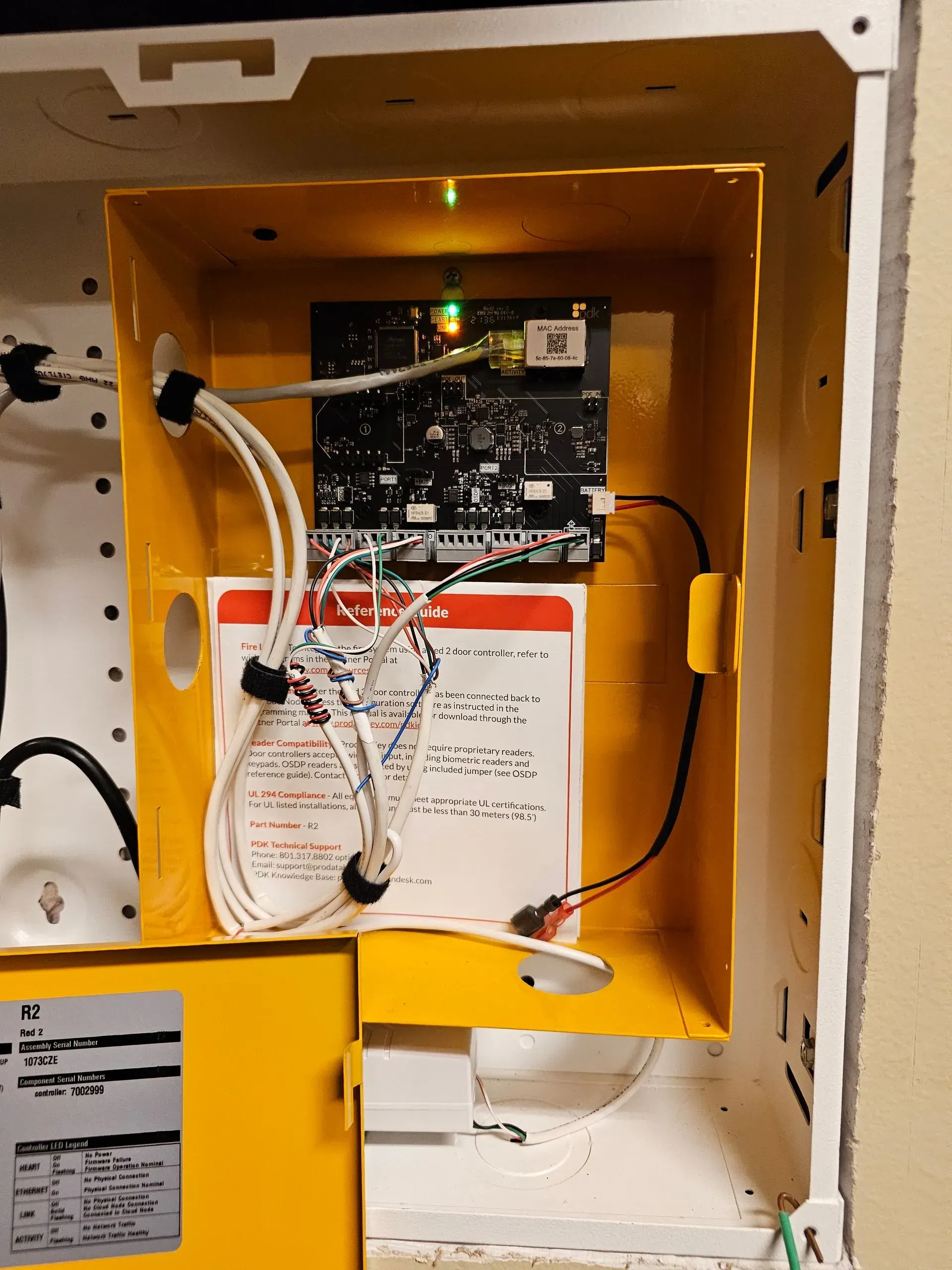 Yellow electrical box with circuit board, wiring, and documentation inside a white enclosure.