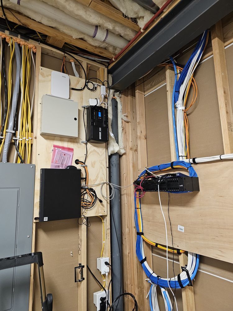 Network and electrical equipment mounted on wooden wall. Cables and conduits are visible.