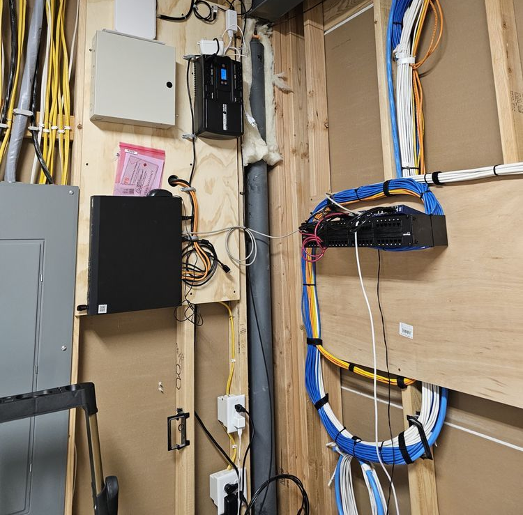 An equipment room with server racks, electrical wiring, and a power outlet mounted on wooden studs.