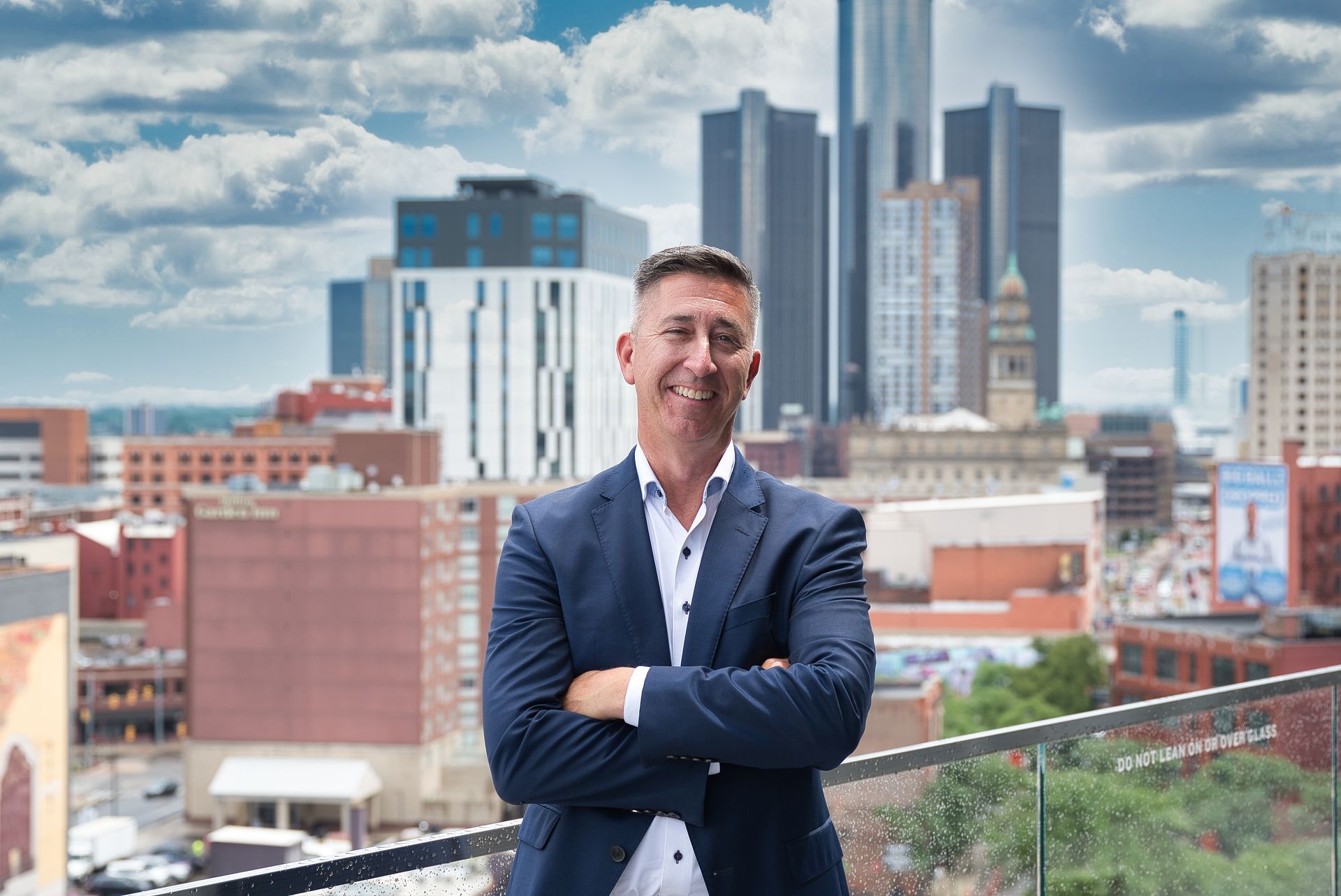 A man in a suit is smiling with his arms crossed.