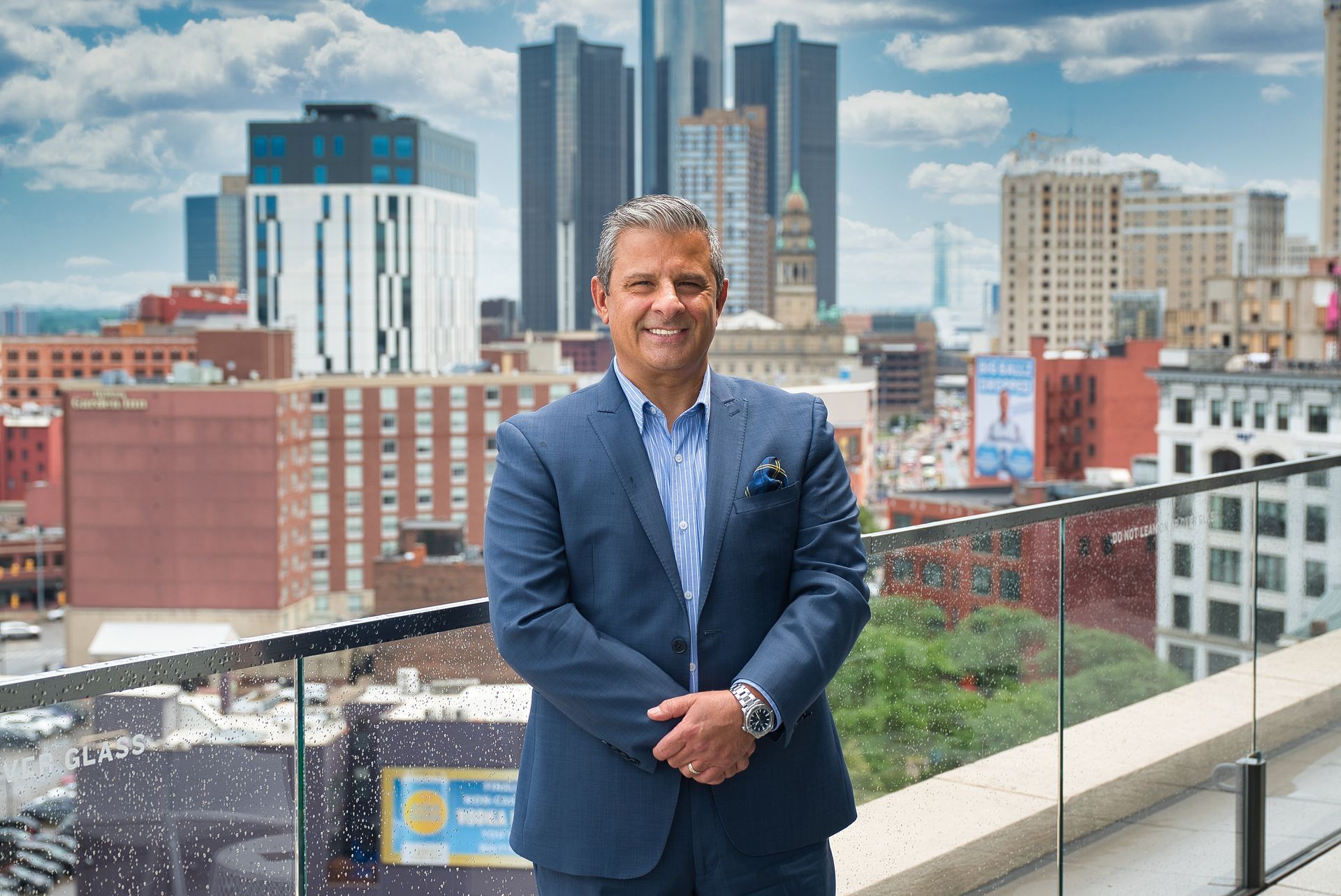 A man in a suit is smiling with his arms crossed.