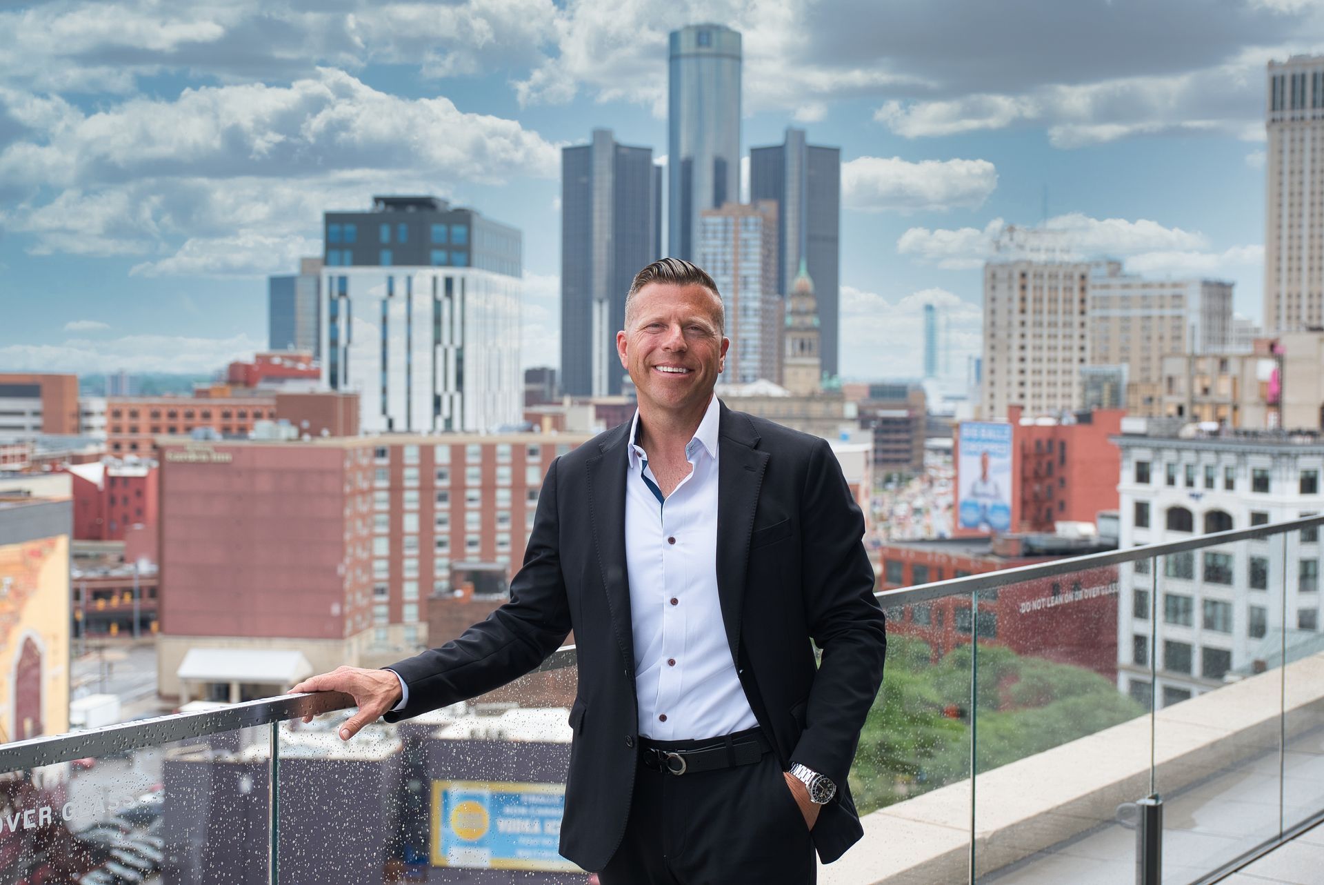 A man in a suit and white shirt is sitting in front of a black background.